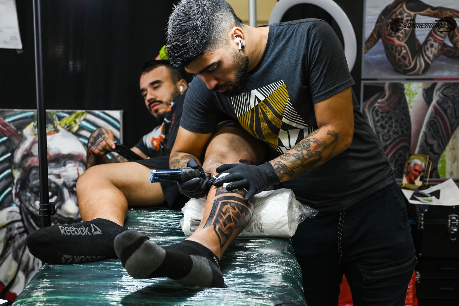 Professional tattoo artists concentrating on intricate designs at a busy convention.