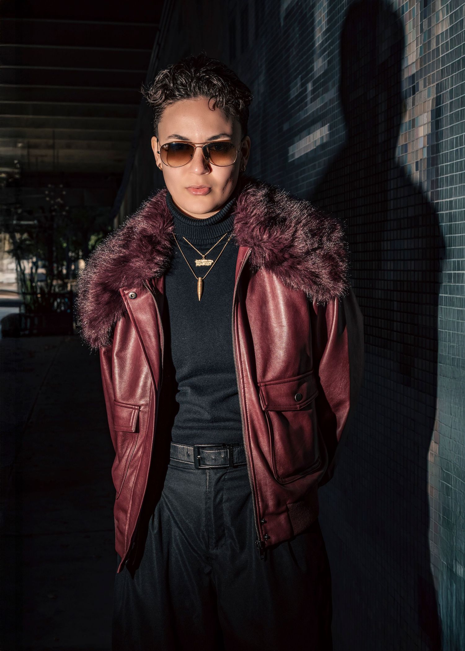 Edgy fashion shoot showcasing burgundy leather jacket with fur trim in dark urban setting.