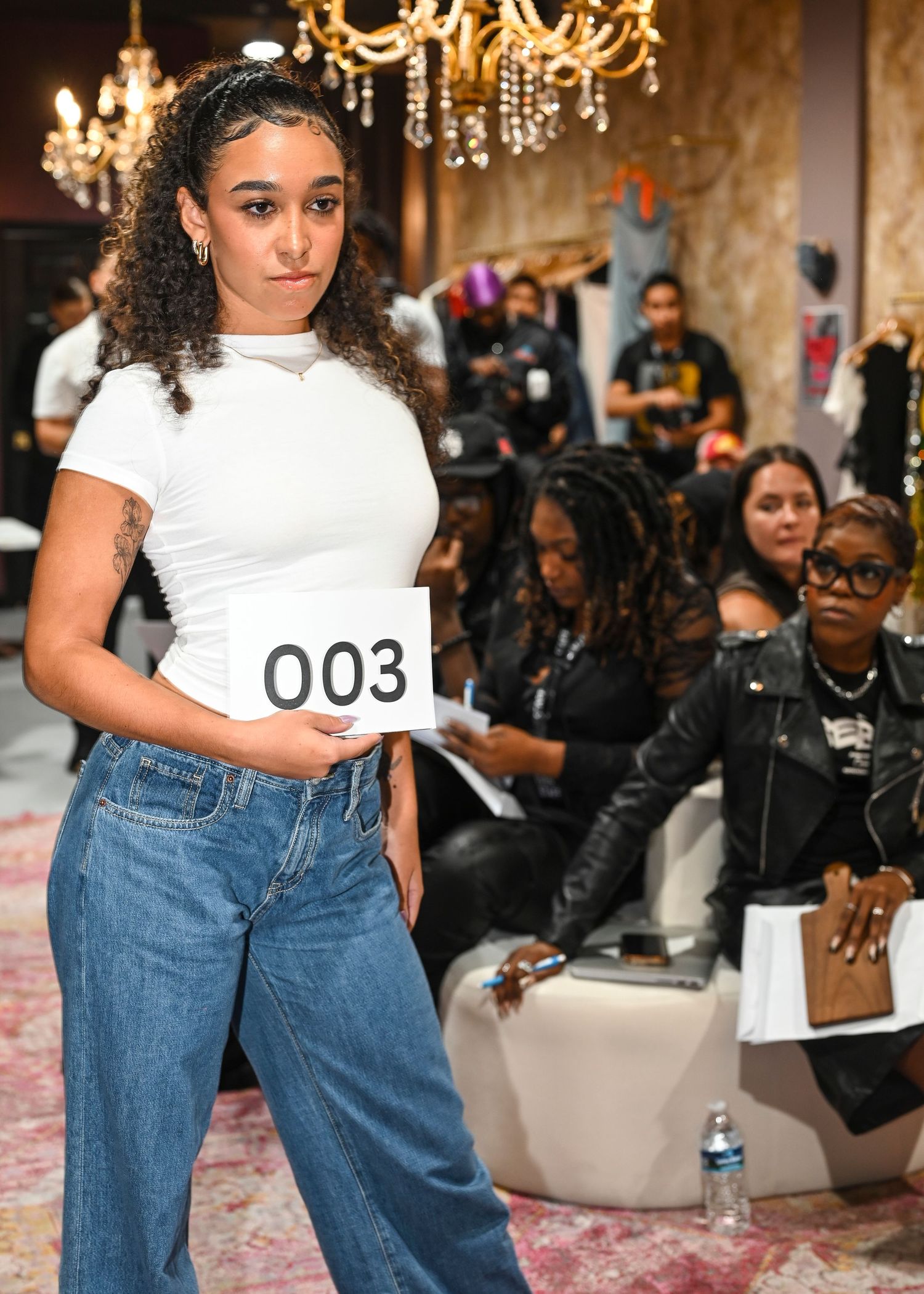 Fashion runway show with models wearing casual denim and white tops under elegant chandeliers.