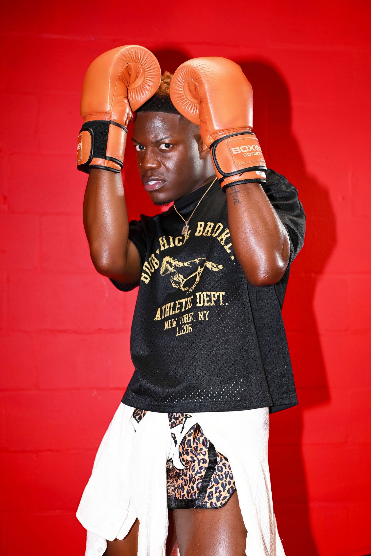 Athletic boxer wearing black and gold jersey throws punches against vibrant red backdrop.