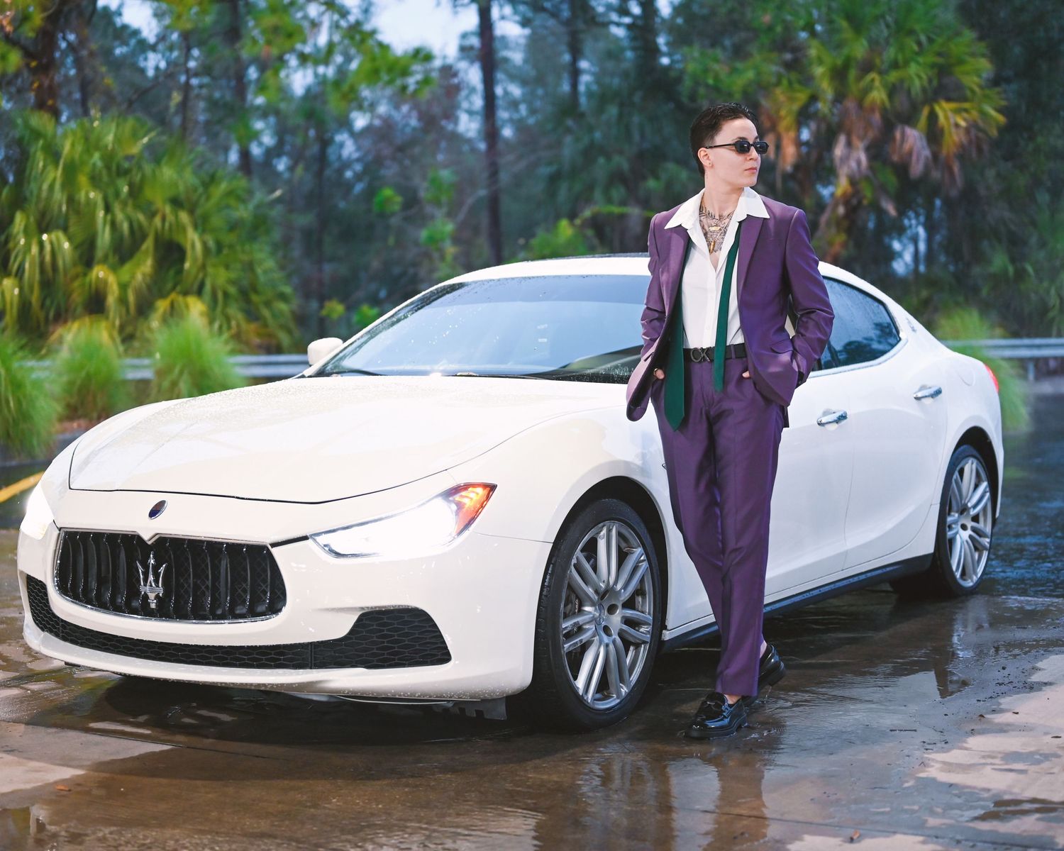 Fashion editorial featuring purple suit and white sports car in wet outdoor setting.
