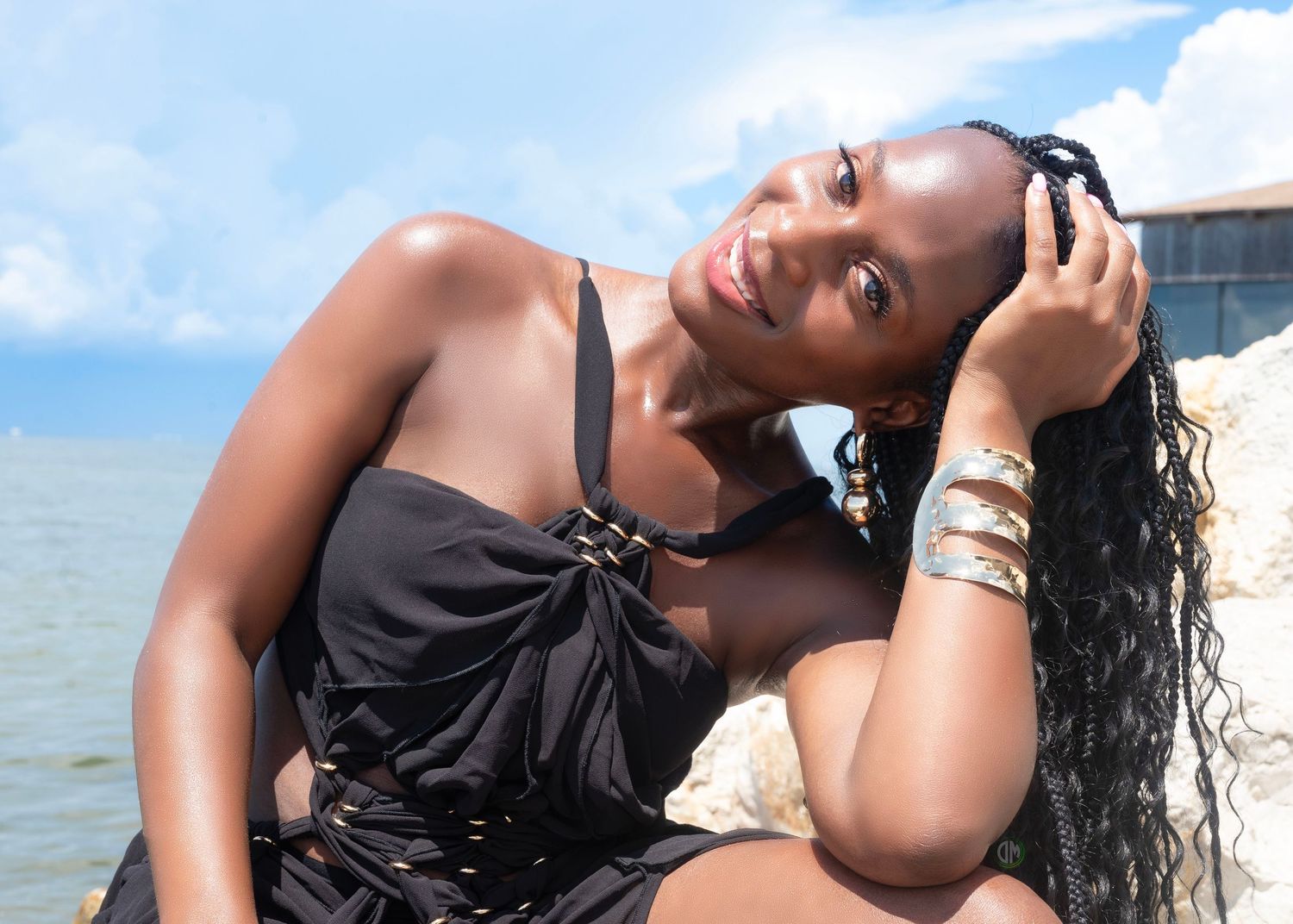 Beach fashion portrait with model in black dress posing against ocean backdrop.