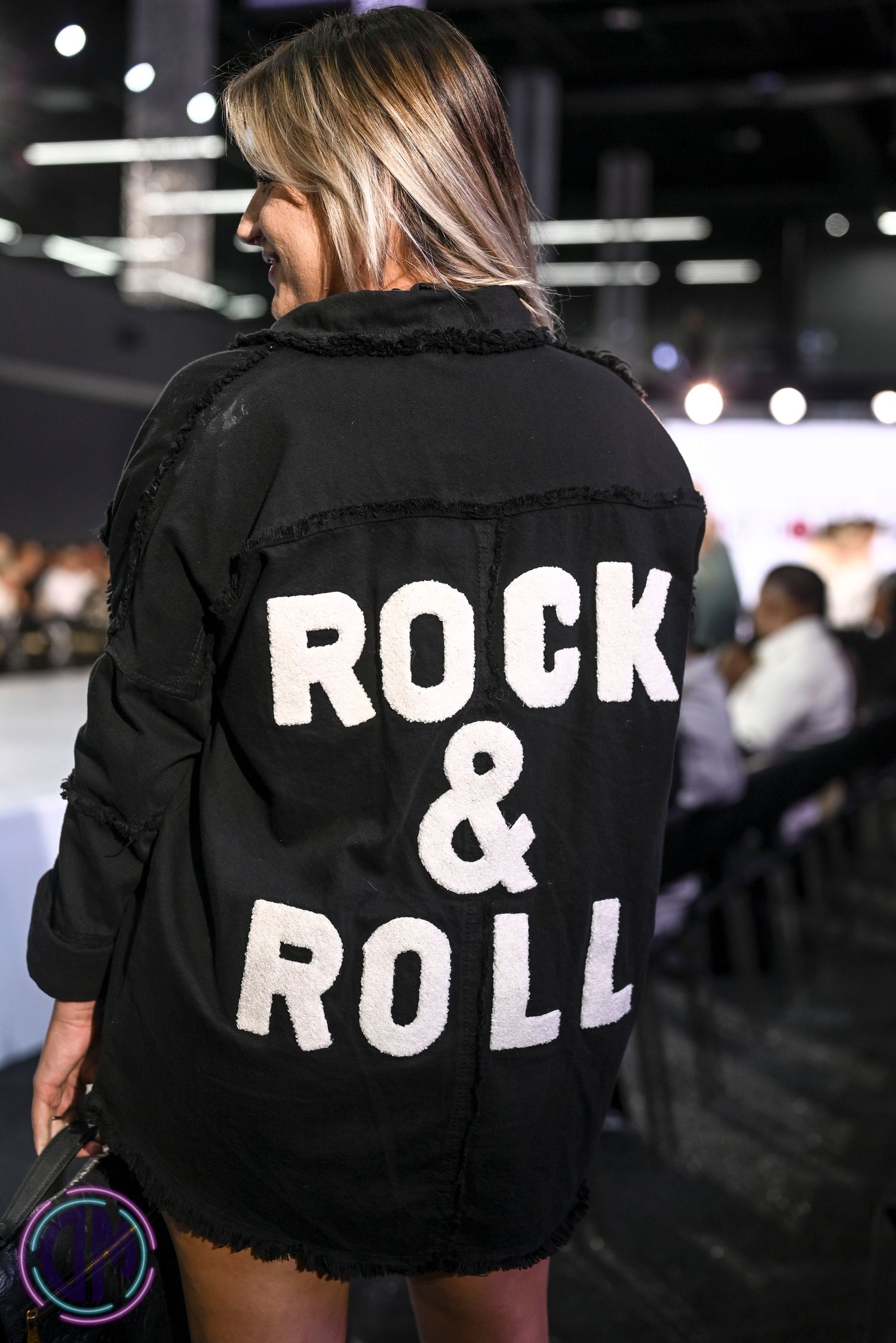 Black denim jacket with 'ROCK & ROLL' text displayed across the back in white lettering on a fashion runway.