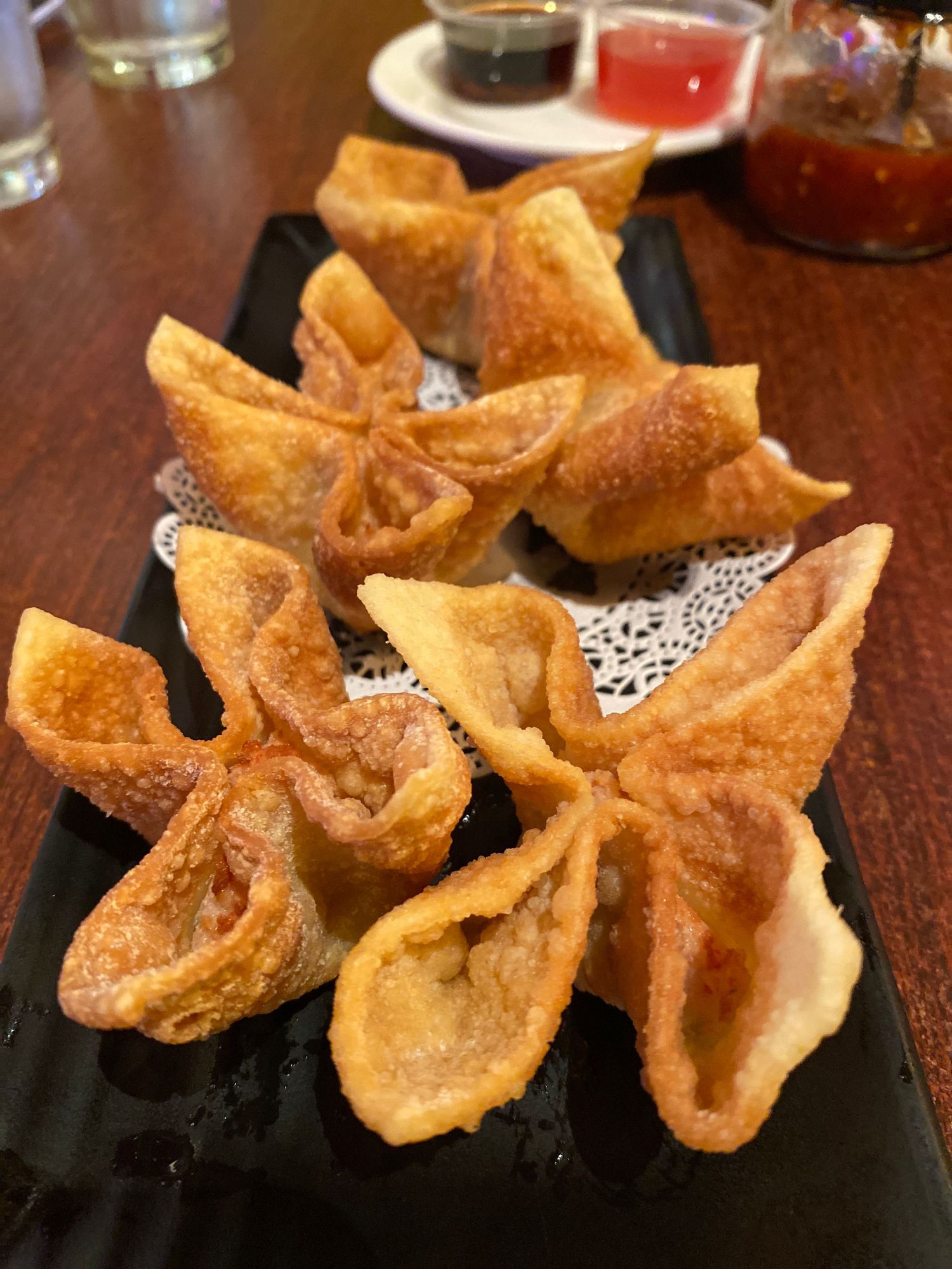 Crispy fried wonton wrappers arranged on a black plate with decorative paper doily.