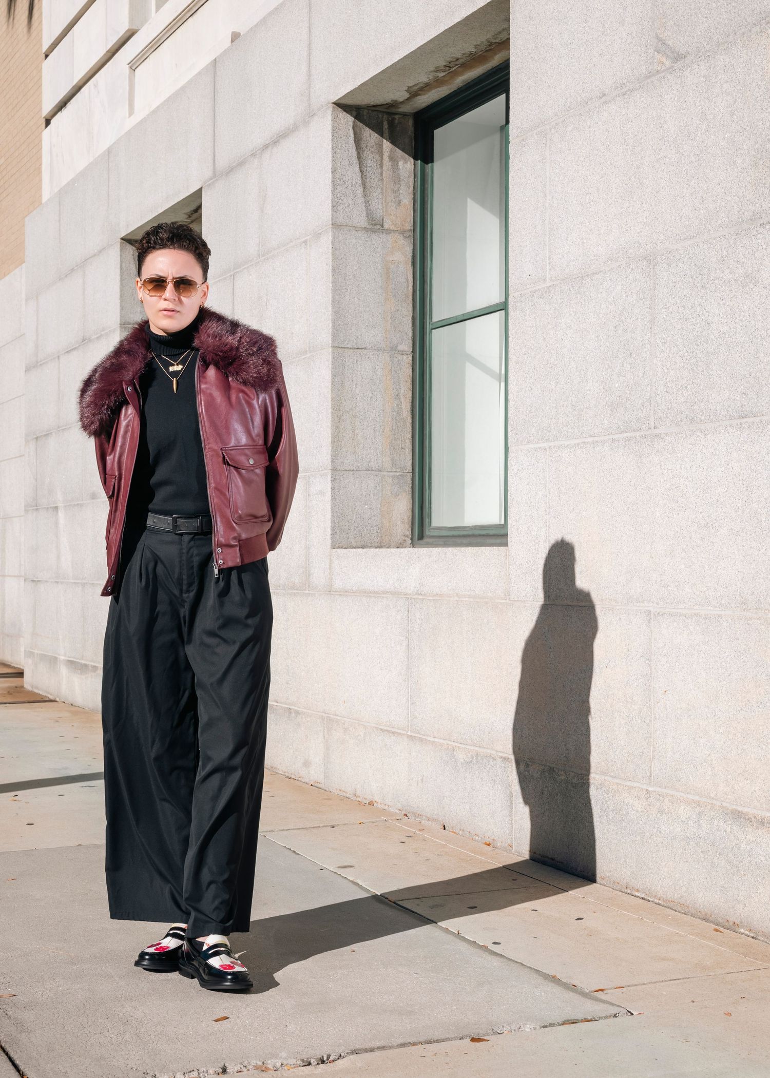 Street style photography featuring black outfit with burgundy jacket against light concrete wall.