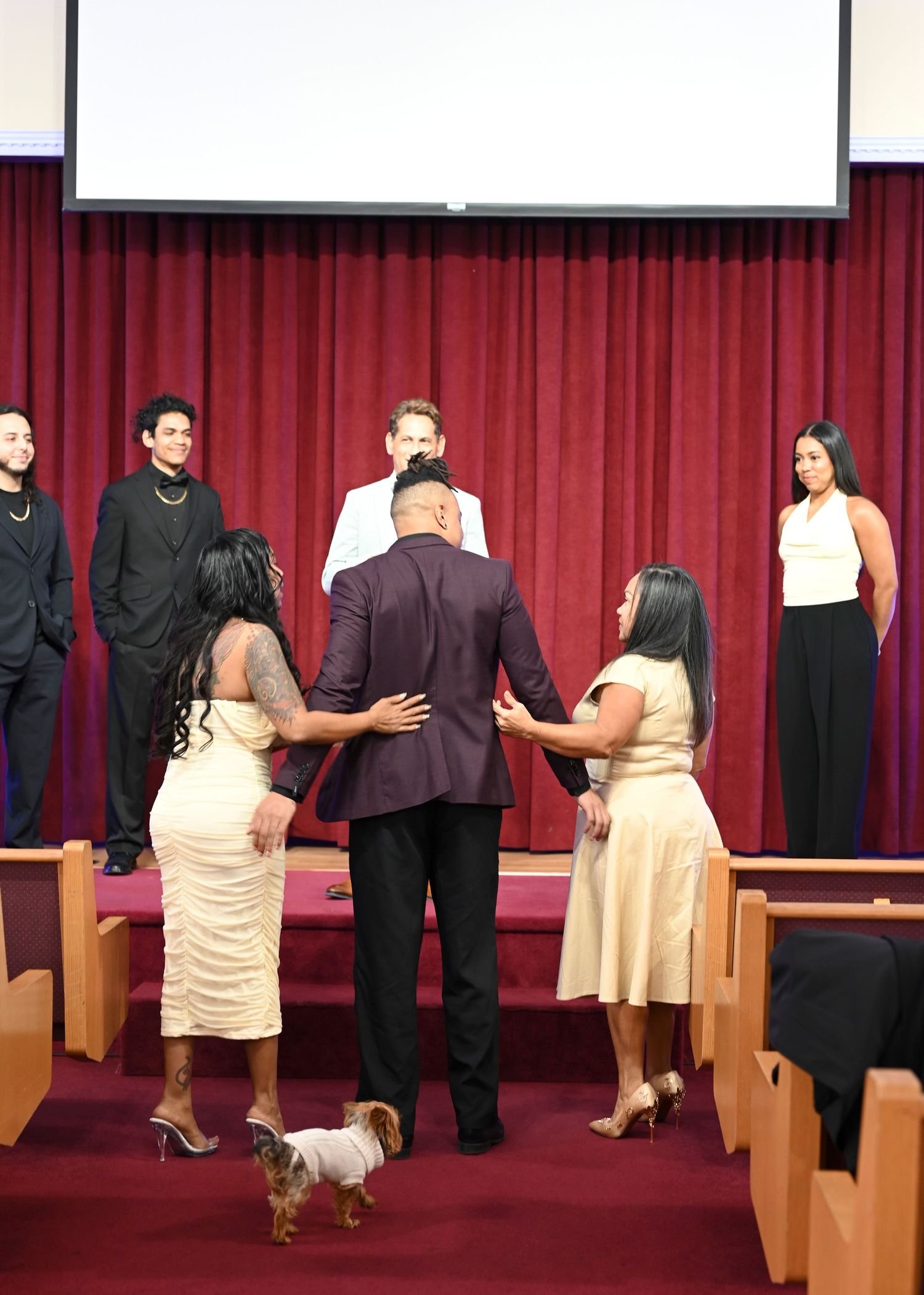 Wedding ceremony in progress with attendees standing near wooden church pews.