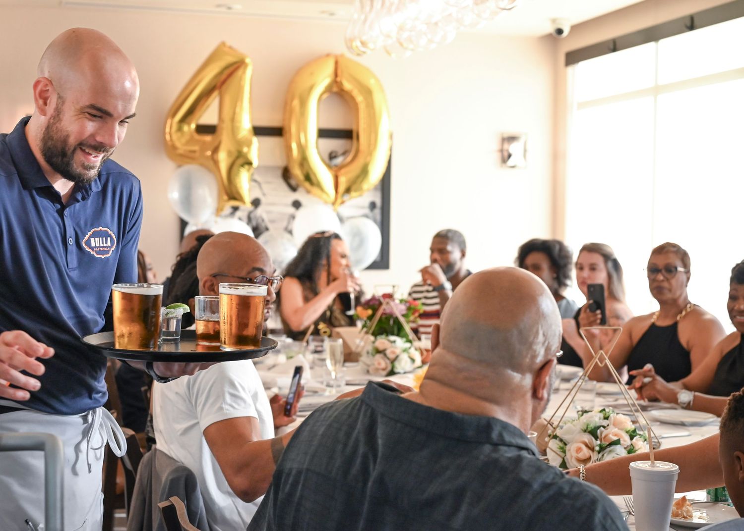 Celebratory gathering with gold number balloons and people dining at restaurant tables.