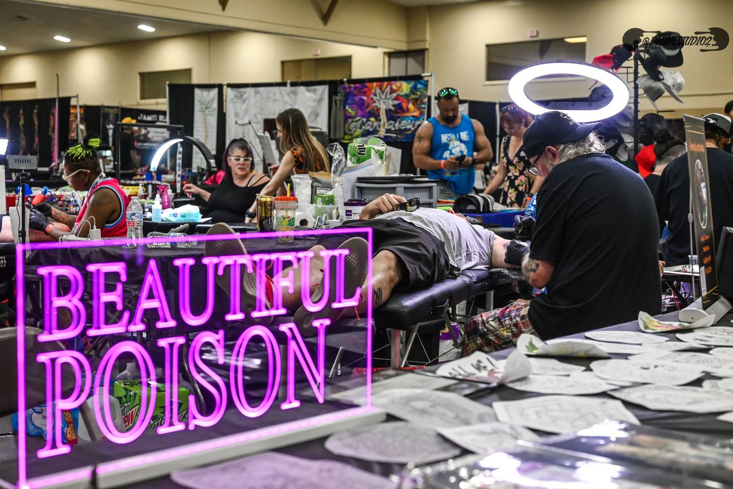 Neon signs and tattoo artists working at stations in a large convention space.