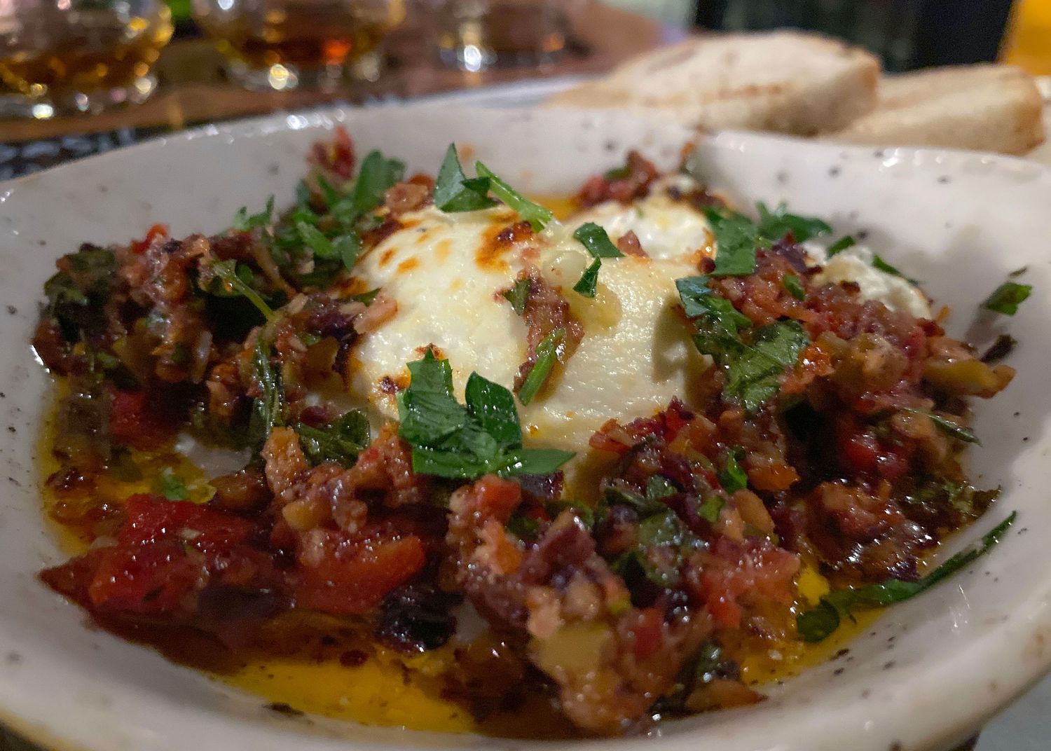 Close-up of braised meat dish with melted cheese and herbs on white plate.