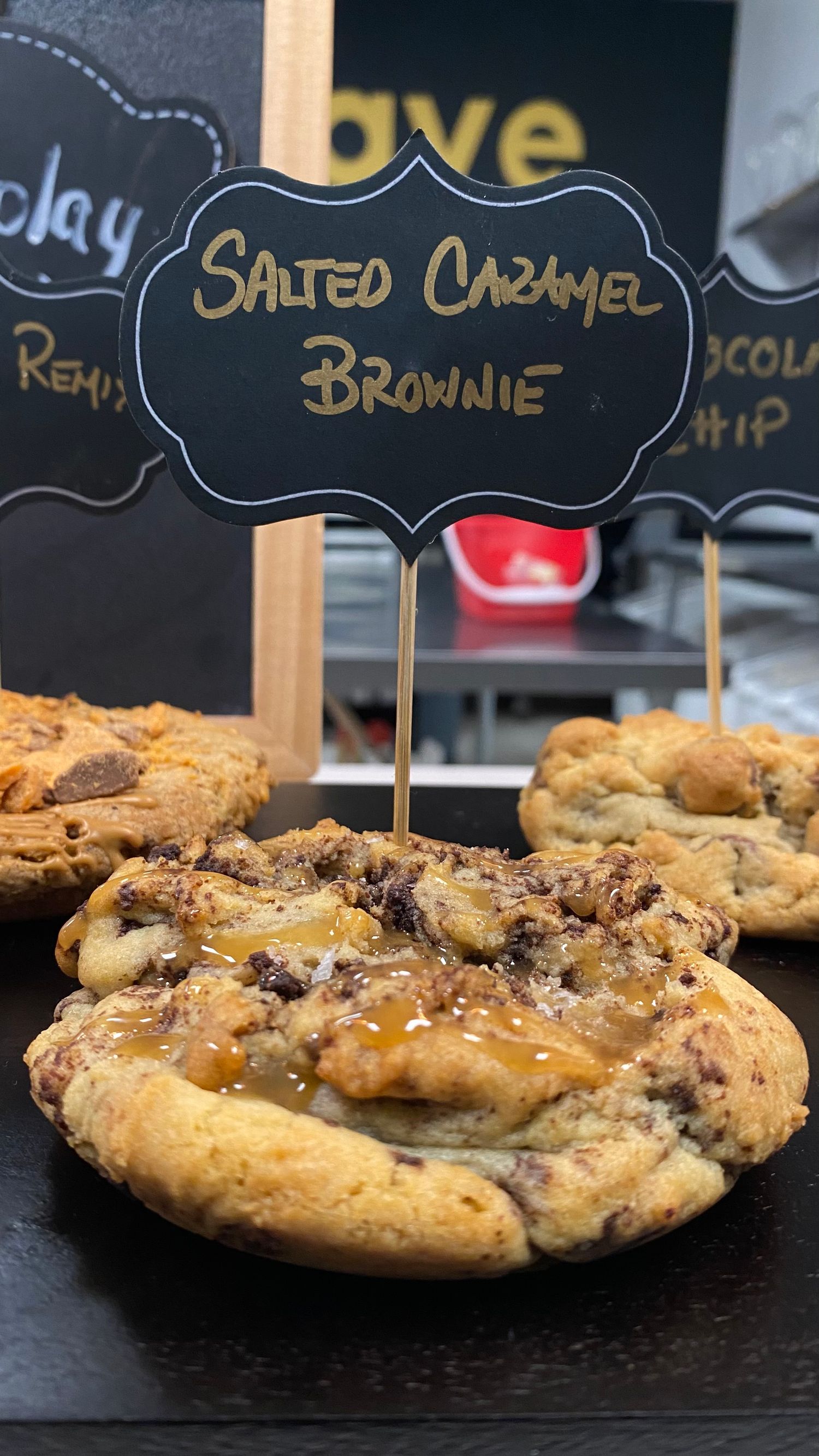 Freshly baked chocolate chip cookies with caramel drizzle and a black name tag display.