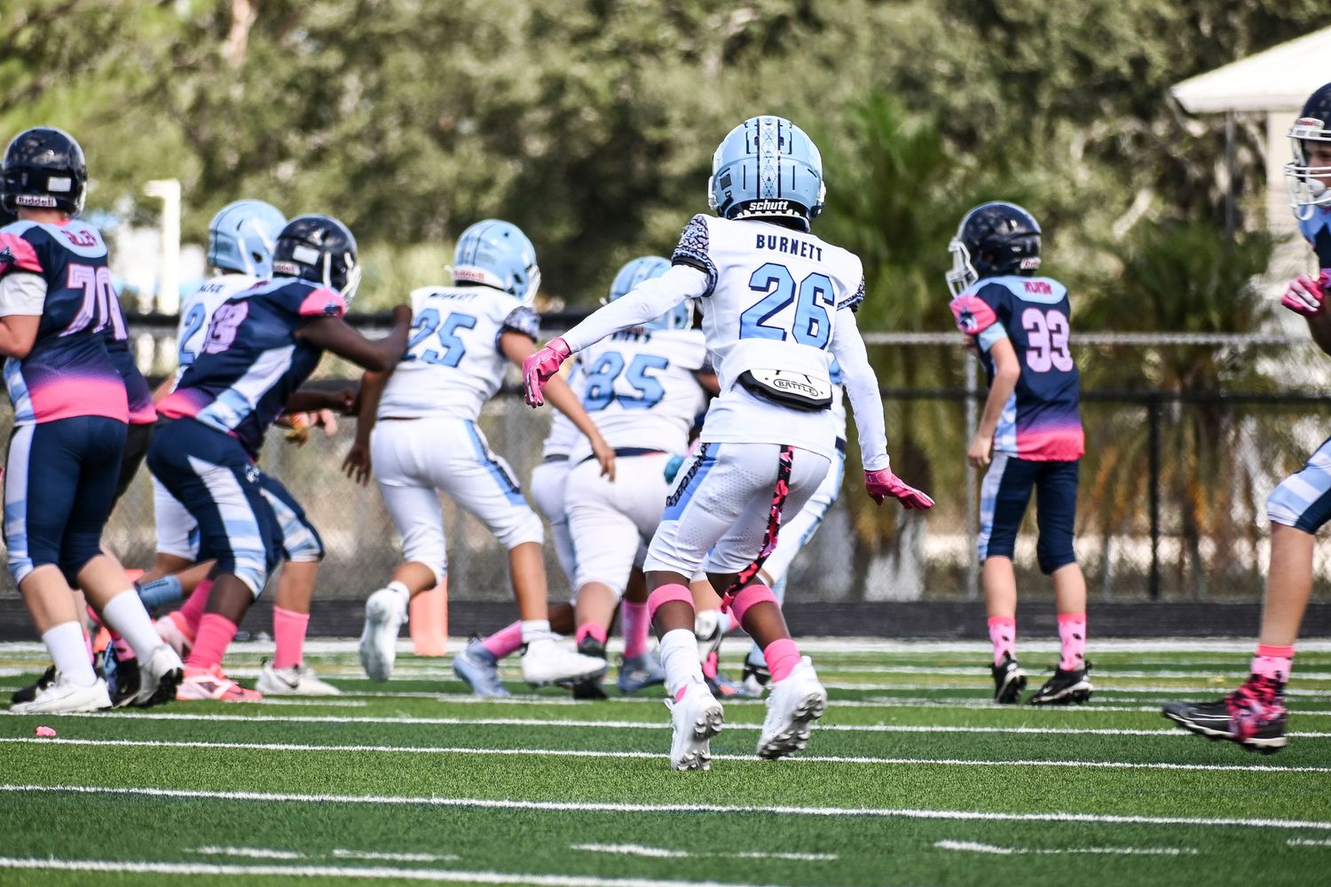 Football team in light blue jerseys practicing formations on grass field.