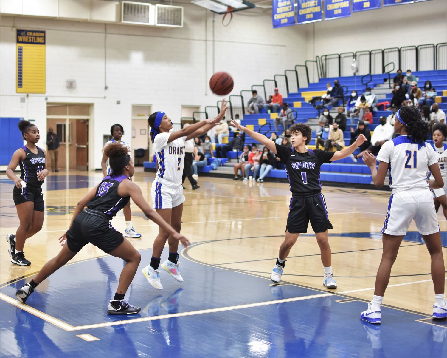 Basketball players jump and stretch during an intense game on a blue indoor court.
