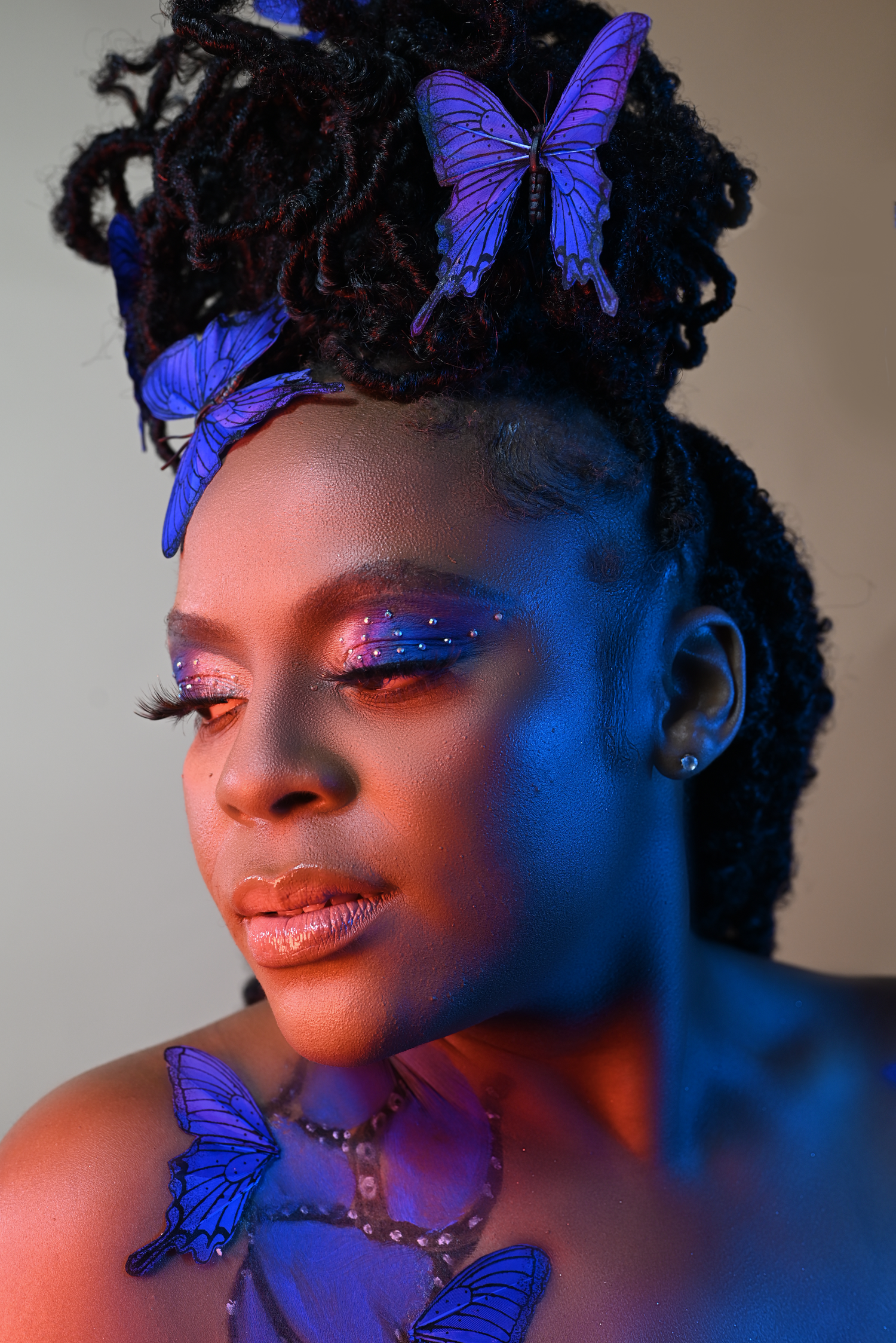 Creative portrait with blue butterflies and glittery makeup in dramatic lighting.