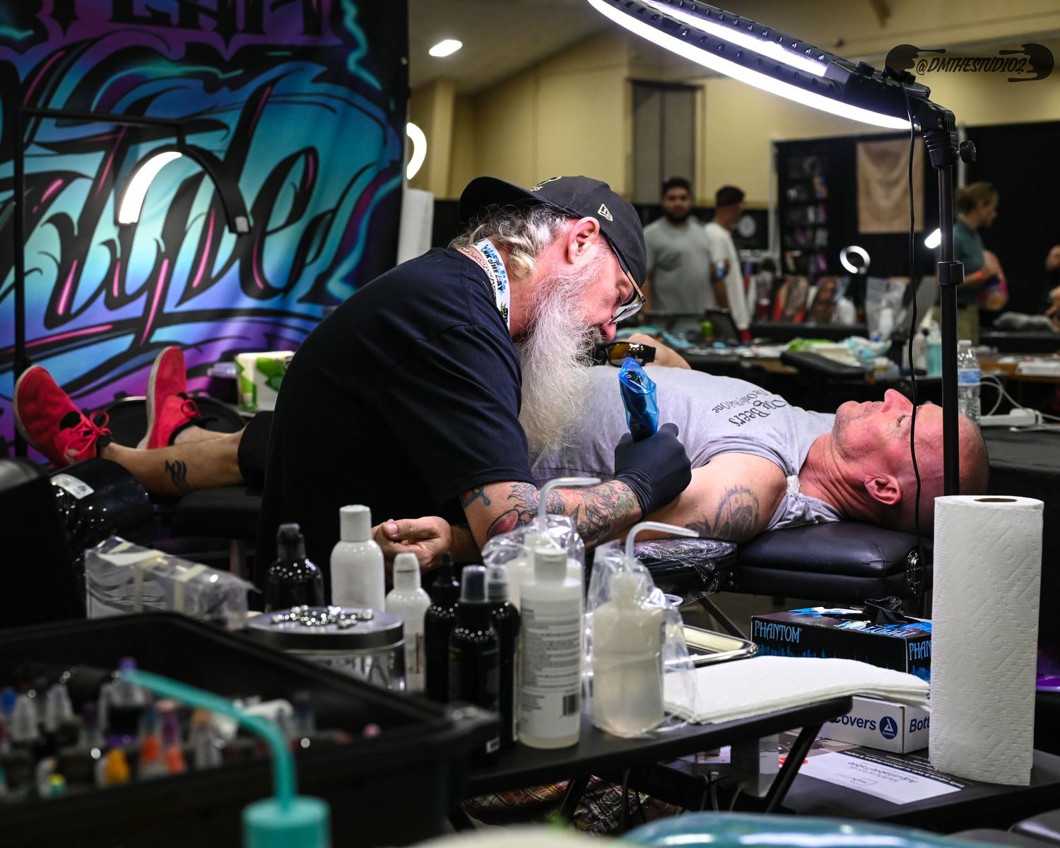 Tattoo artists working at illuminated stations with professional equipment and supplies.