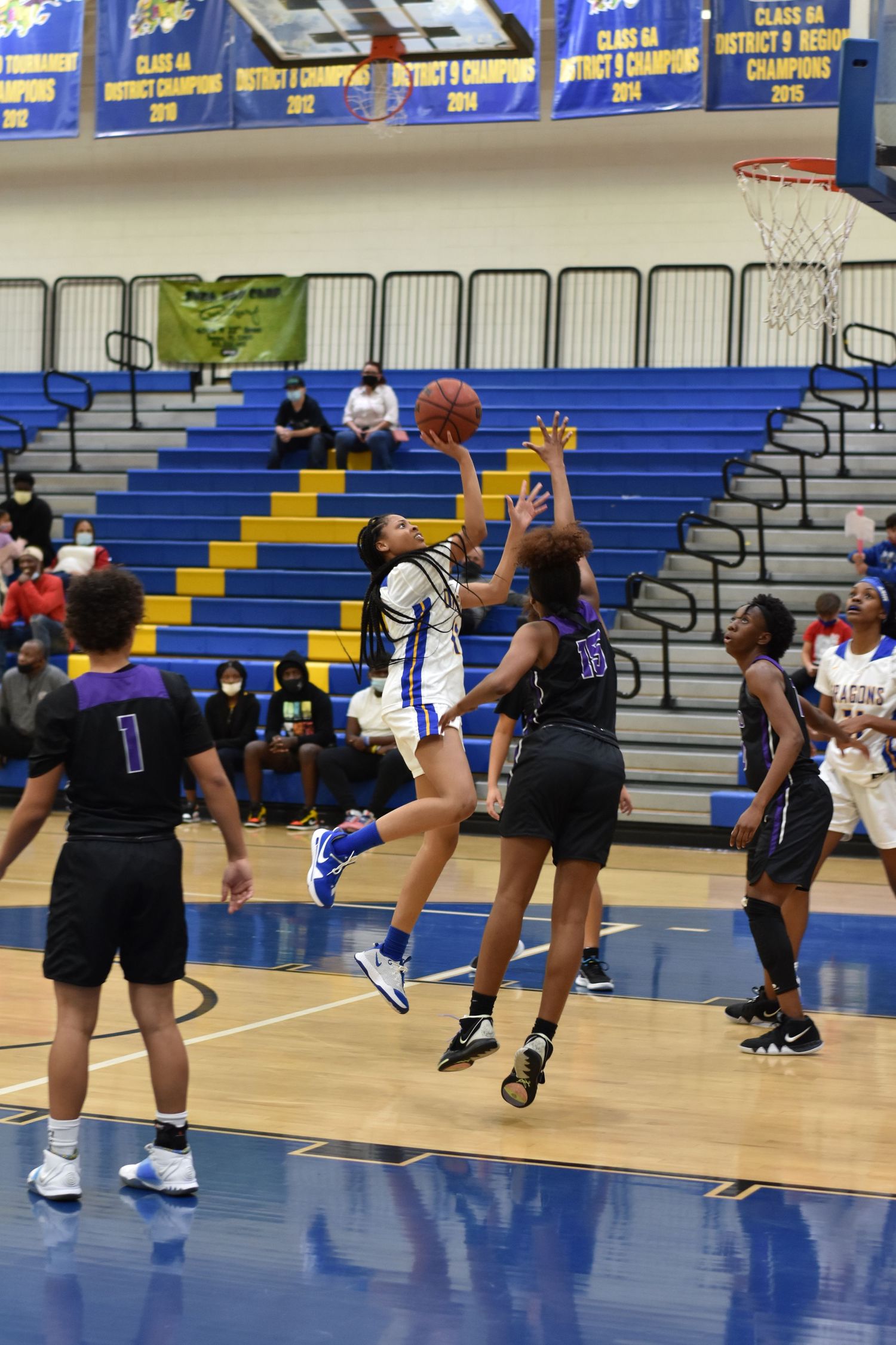 Basketball players in black uniforms positioning for a rebound under the hoop.