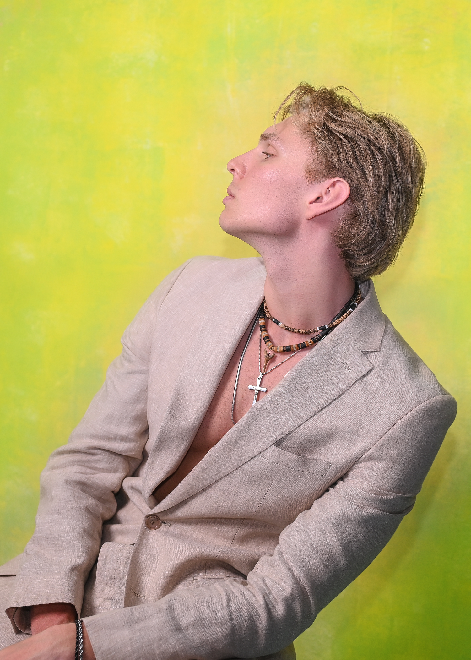 Person in gray suit jacket posing dramatically against yellow-green background.