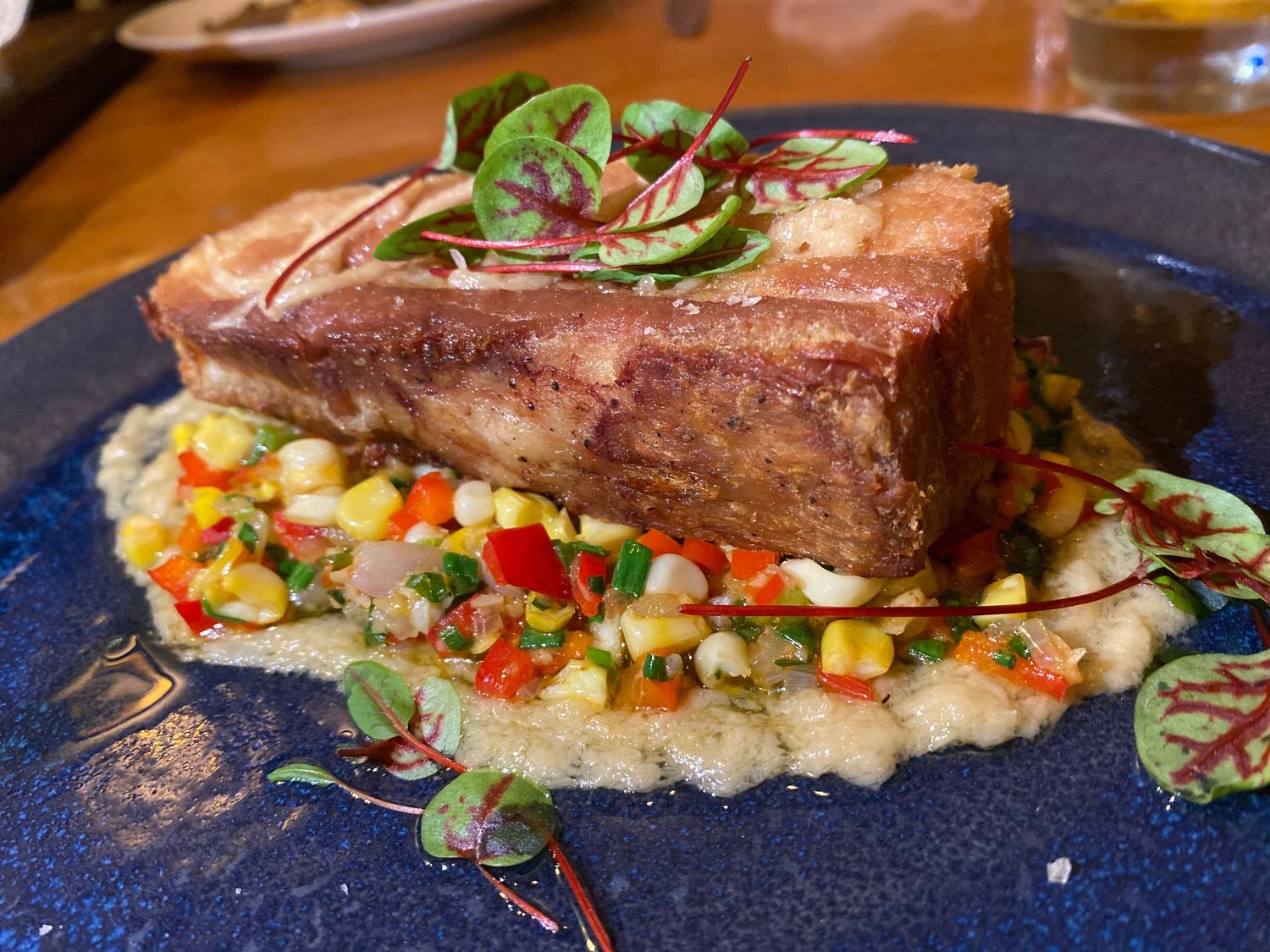 Braised pork belly served on a bed of colorful corn succotash on a blue plate.