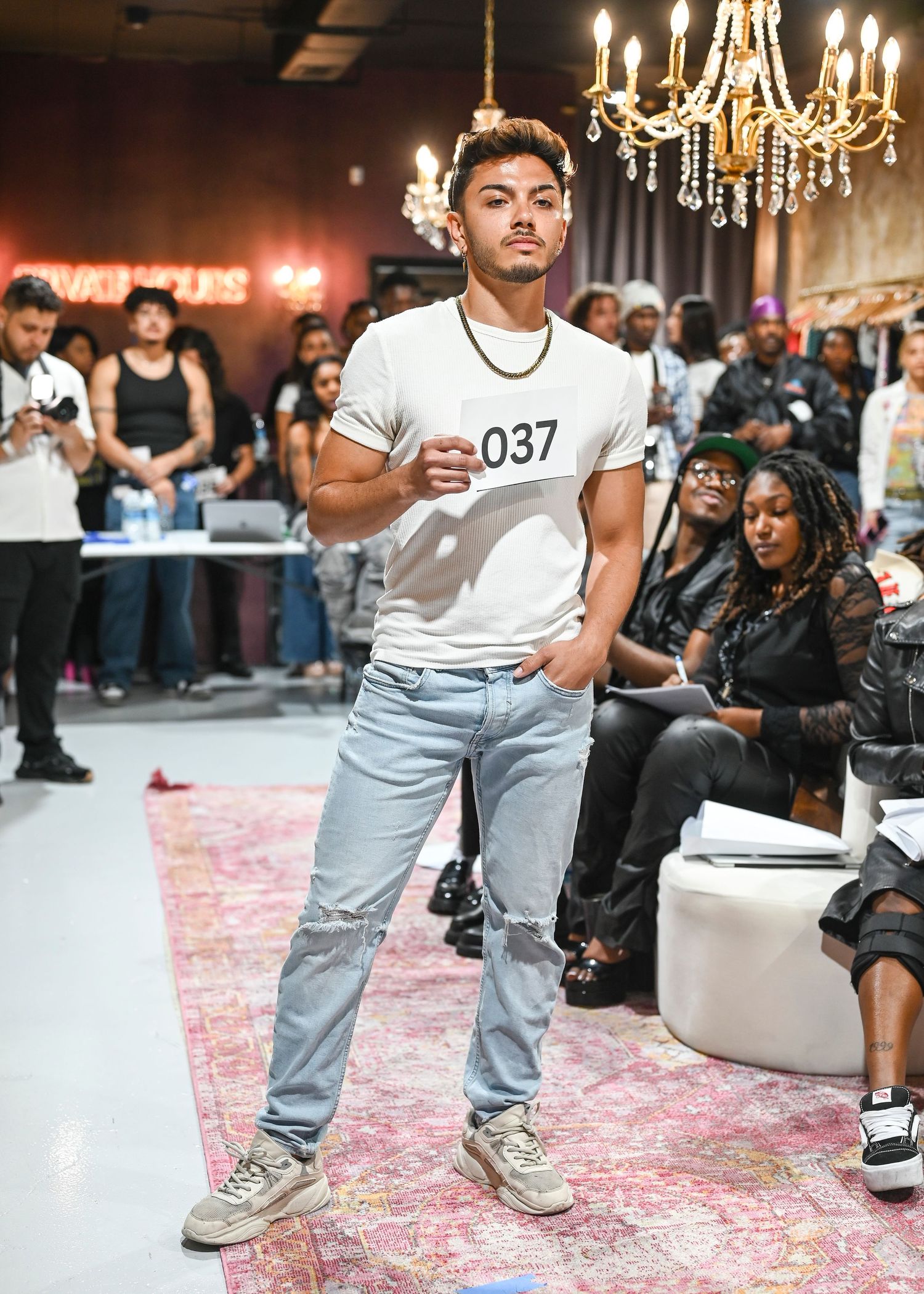 Models showcase casual streetwear looks under elegant lighting on a pink runway.