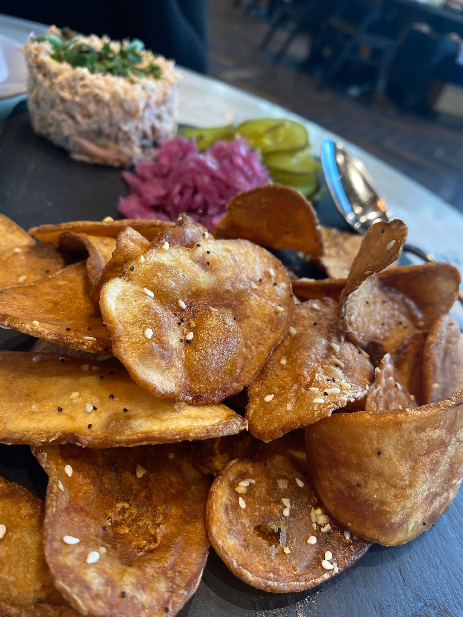 Crispy homemade potato chips served with pickled onions and a creamy dip on a dark slate plate.