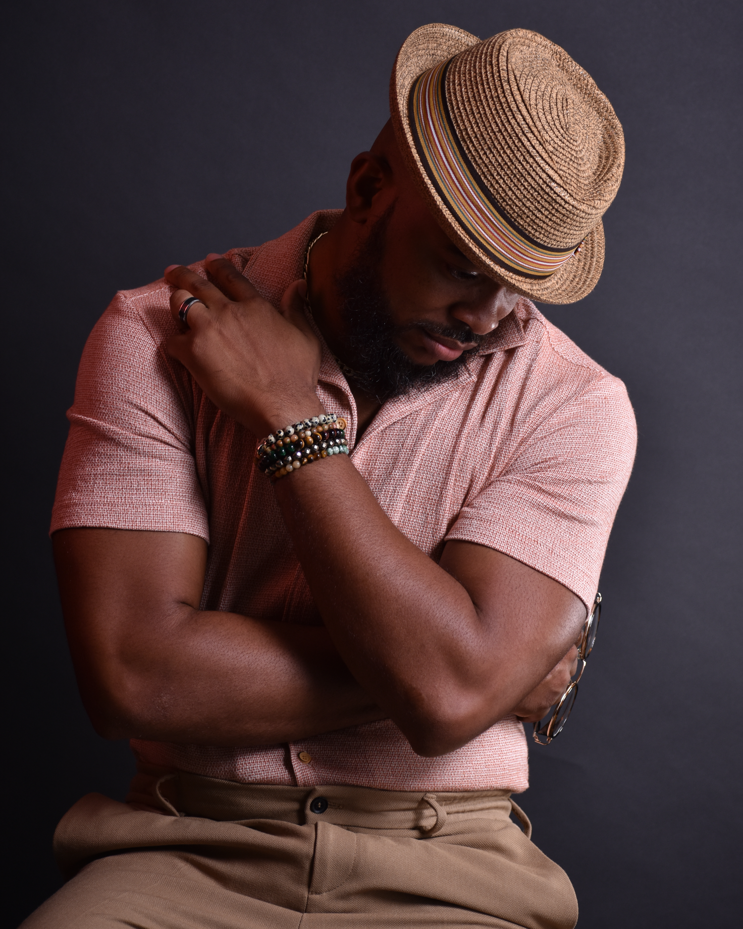 Artistic portrait of model in pink shirt and straw hat posing against dark background.