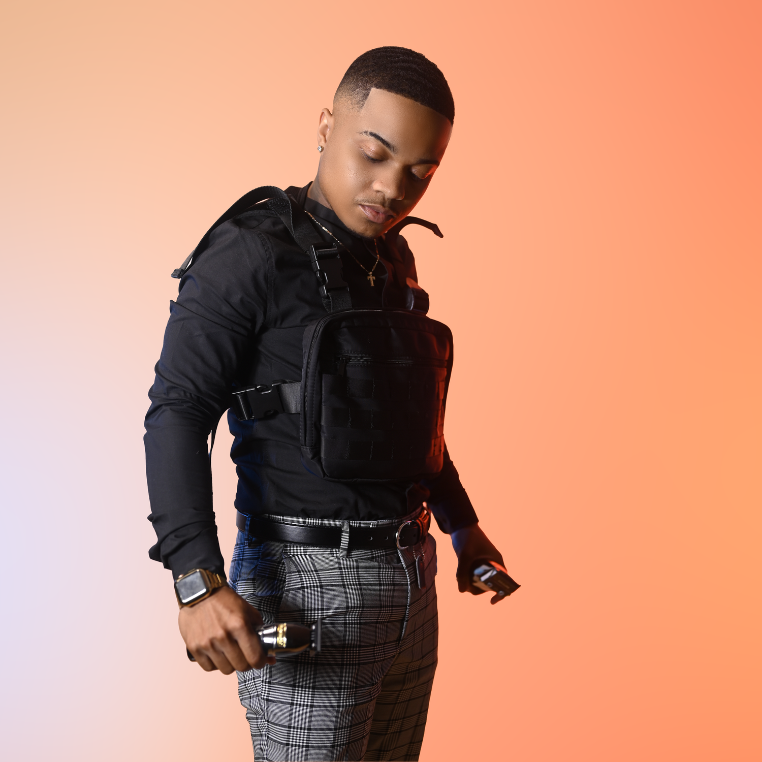 Fashion portrait of someone wearing tactical black clothing and plaid pants against coral background.