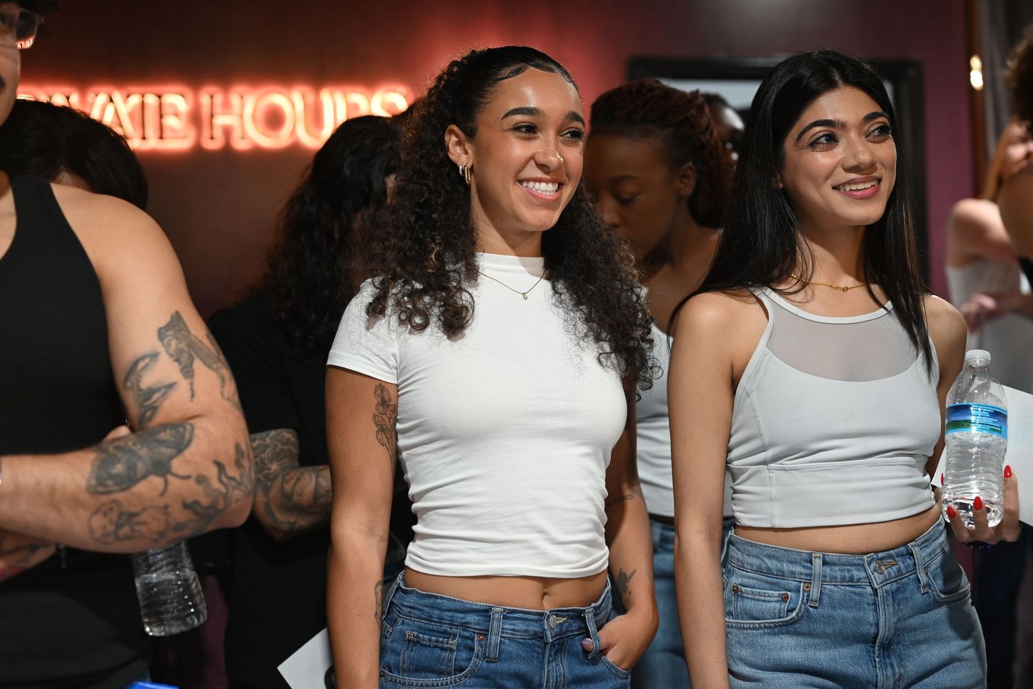 Diverse crowd gathered at an indoor event wearing casual summer outfits and white tops.