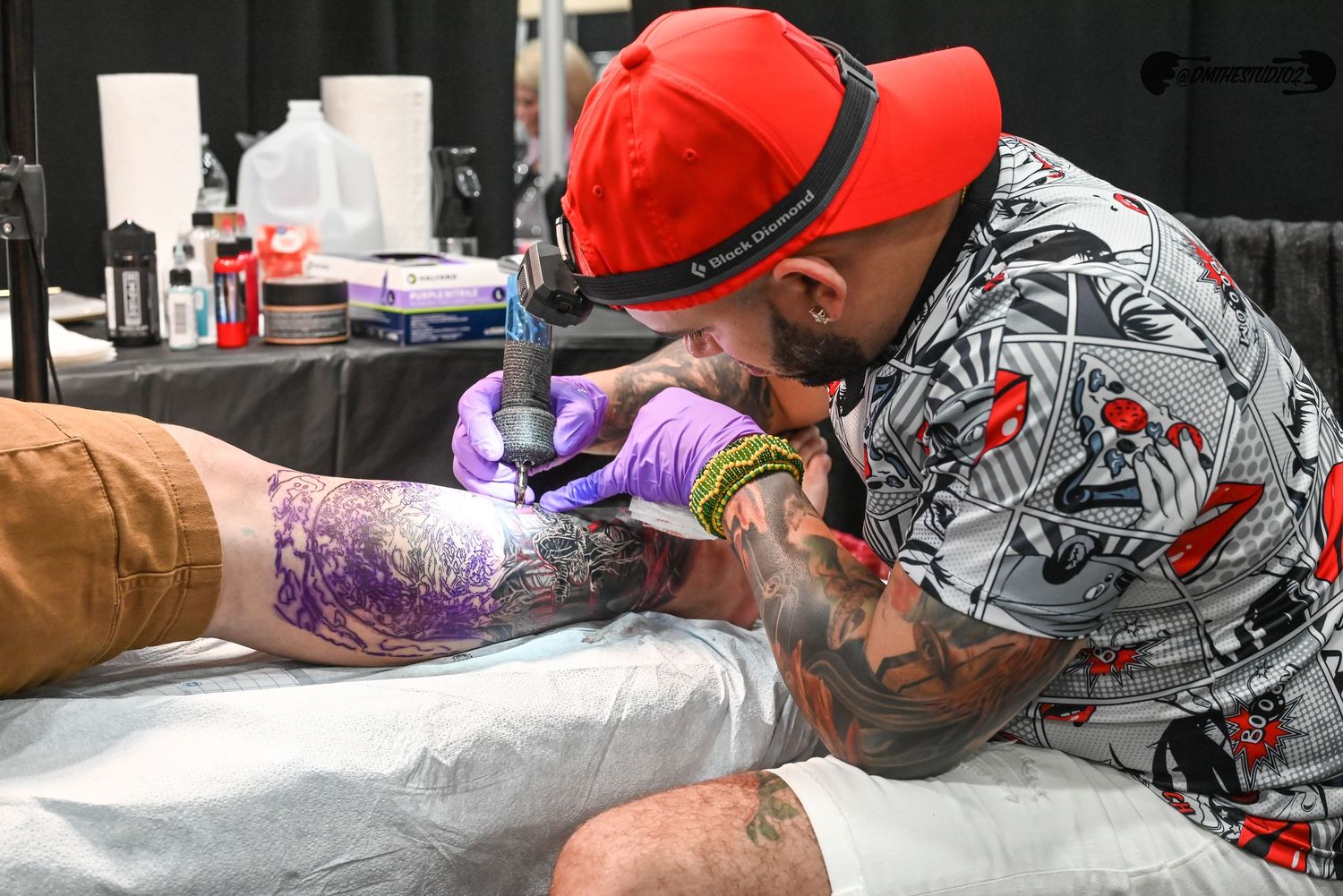 Multiple tattoo artists in red caps working on clients at a busy convention.