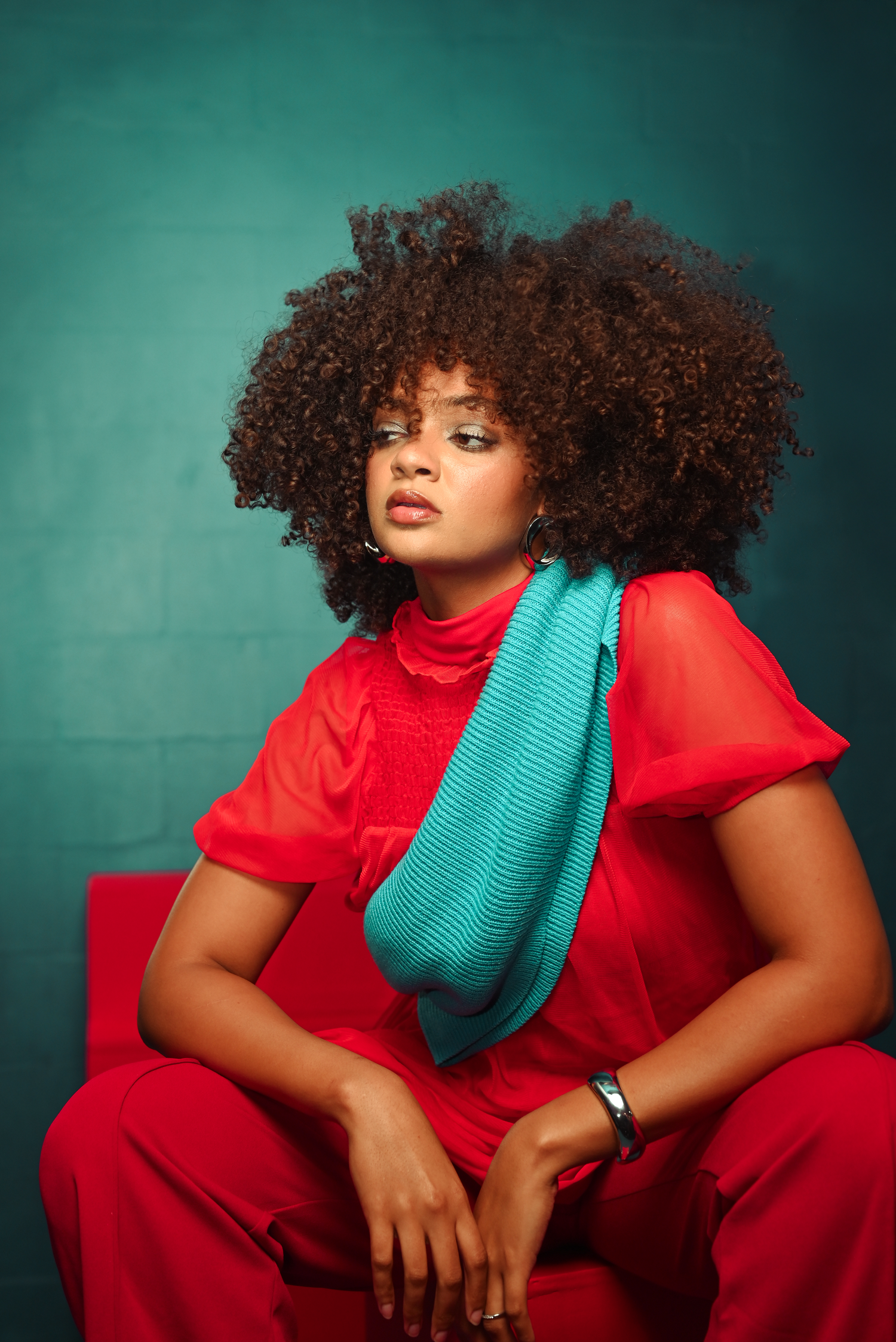 Artistic portrait series with natural curls in red outfit against teal backdrop.