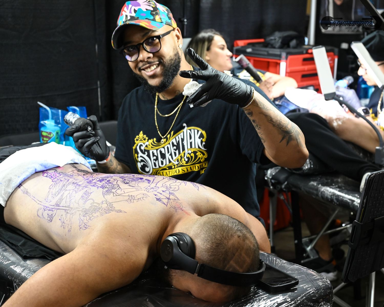Tattoo artists applying designs while wearing protective gear at convention booths.
