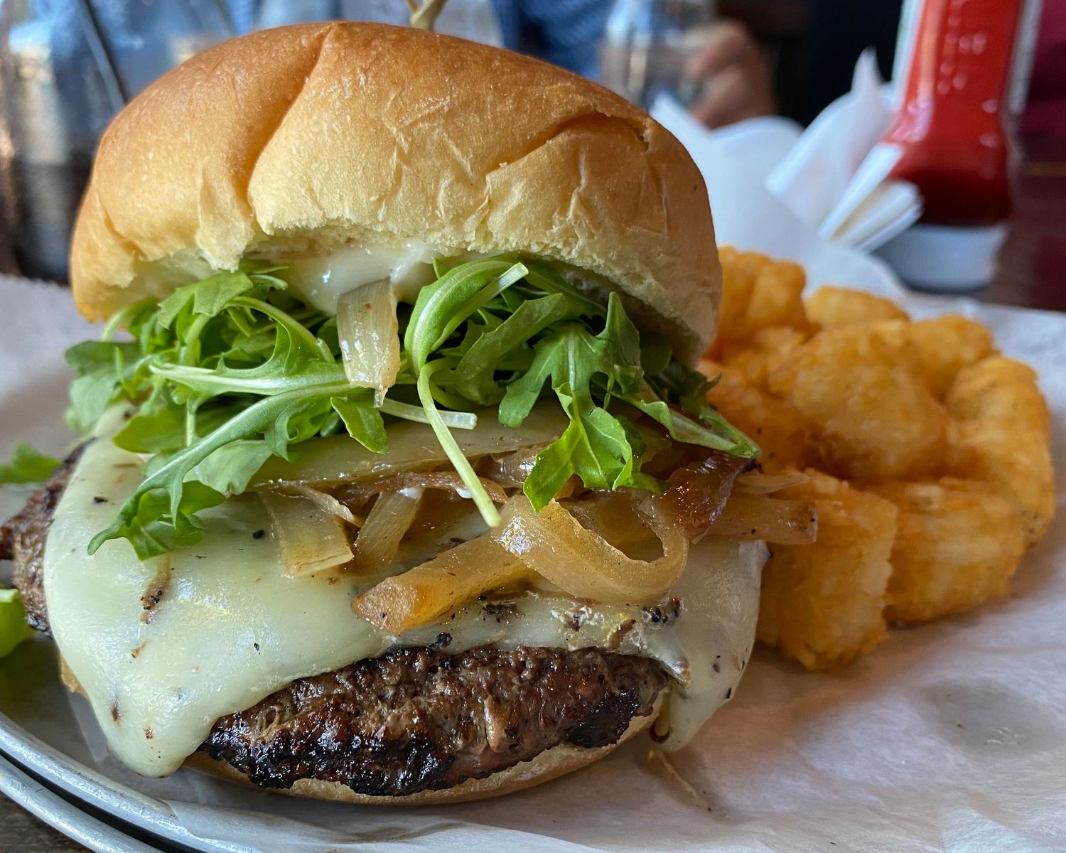 Gourmet burger with melted cheese, lettuce, and onion rings served with fries.