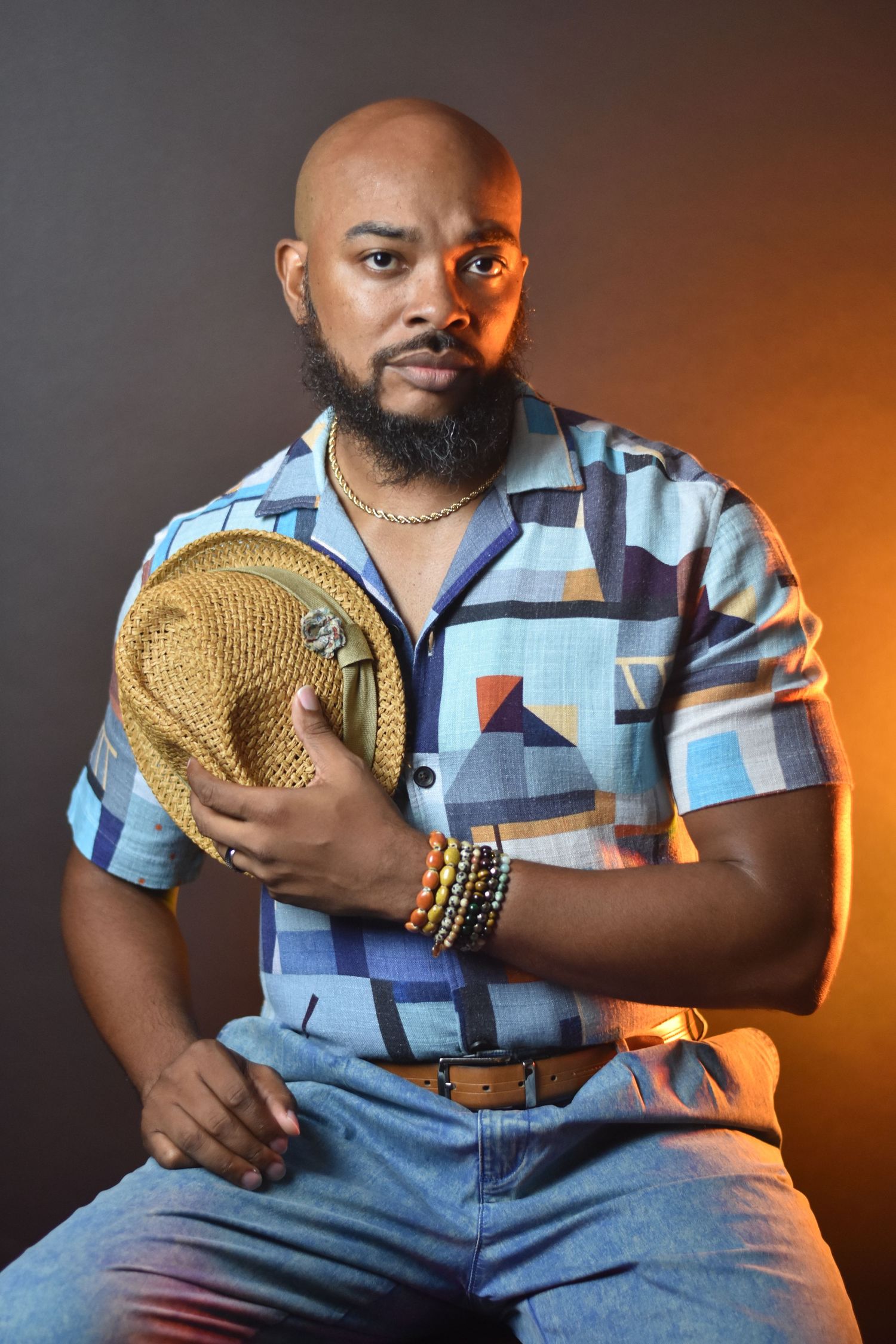 Portrait session featuring blue patchwork shirt and straw hat with dramatic orange lighting.
