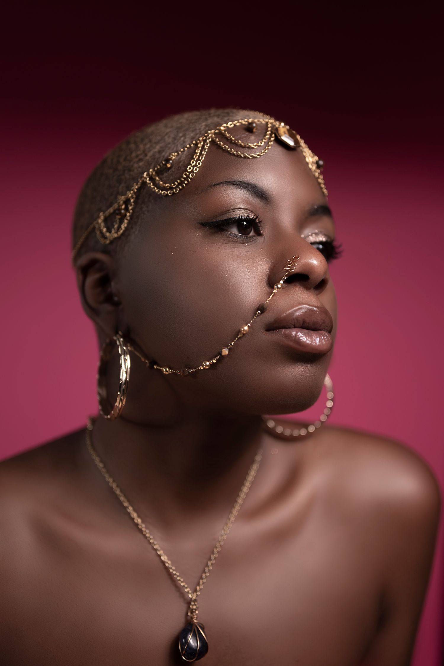 Artistic beauty portrait with gold chain accessories against burgundy background.