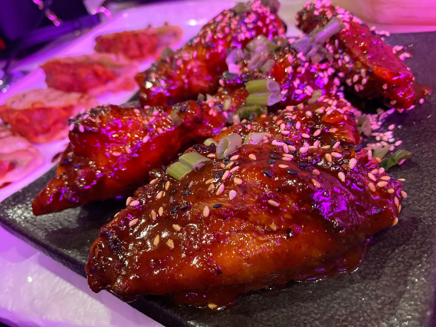 Glazed chicken wings with sesame seeds under purple ambient lighting.