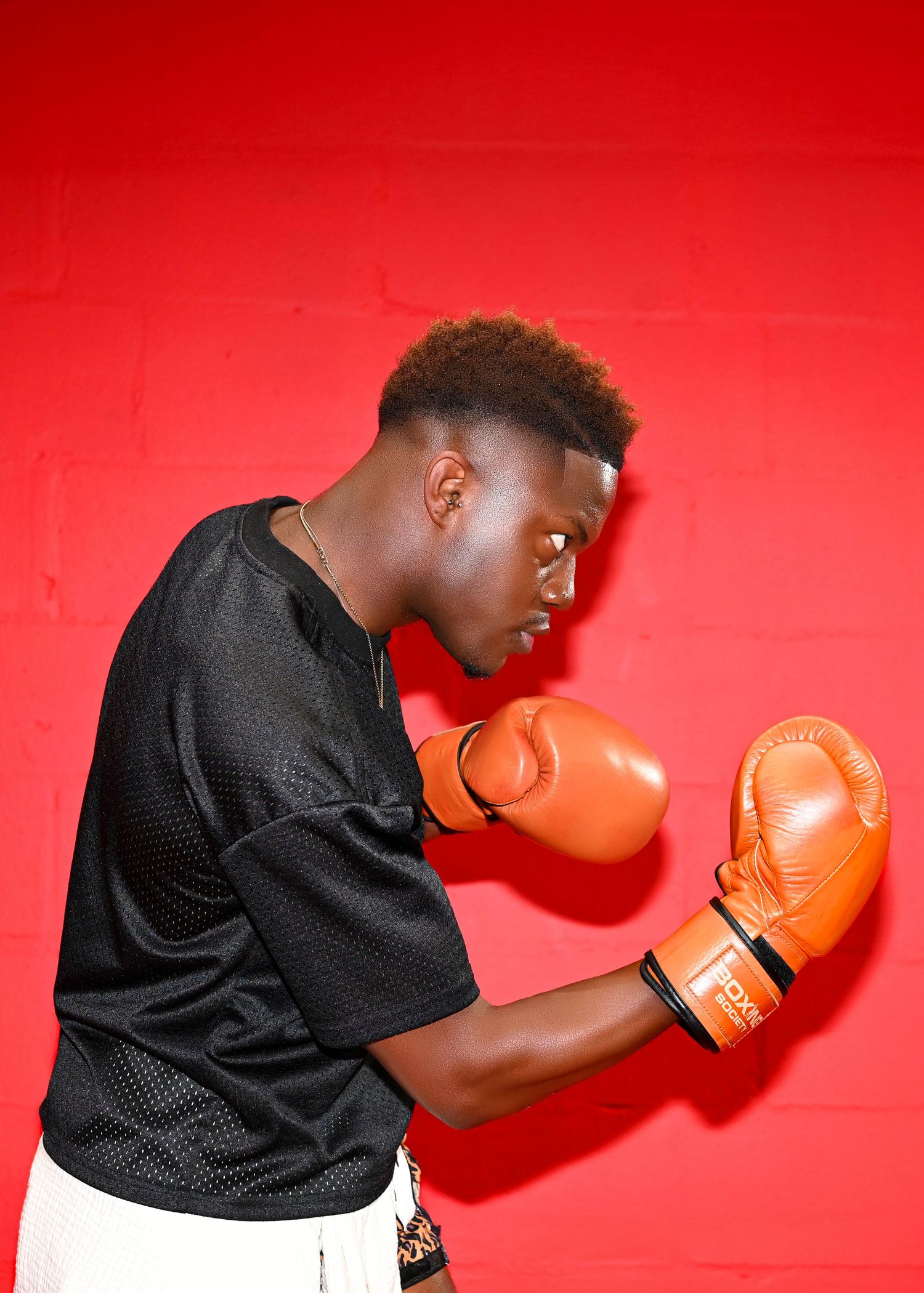 Dynamic boxing sequence shows athlete throwing punches in training gear against red wall.