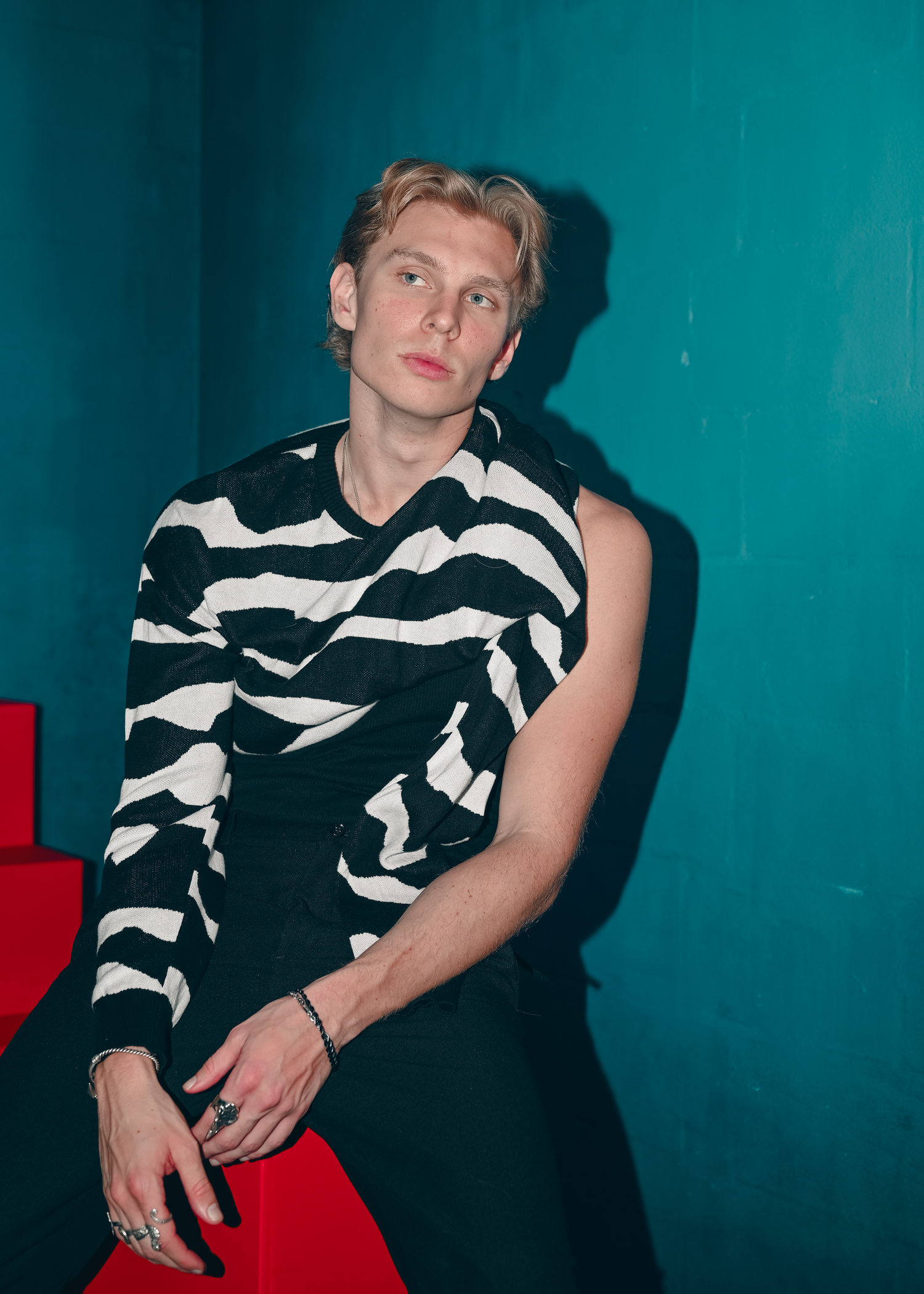 Model in black and white striped shirt poses dramatically against teal background.