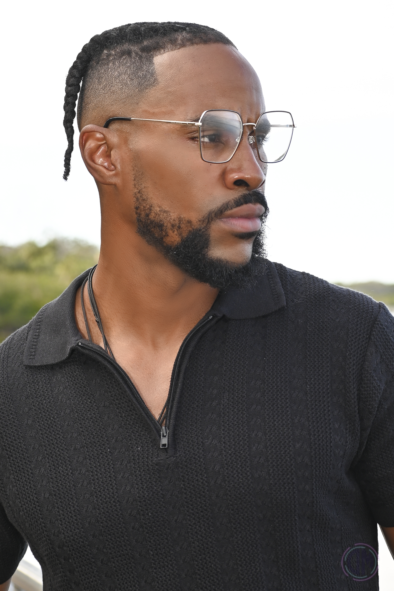 Outdoor portrait of someone in a black quarter-zip sweater and aviator glasses with natural lighting.