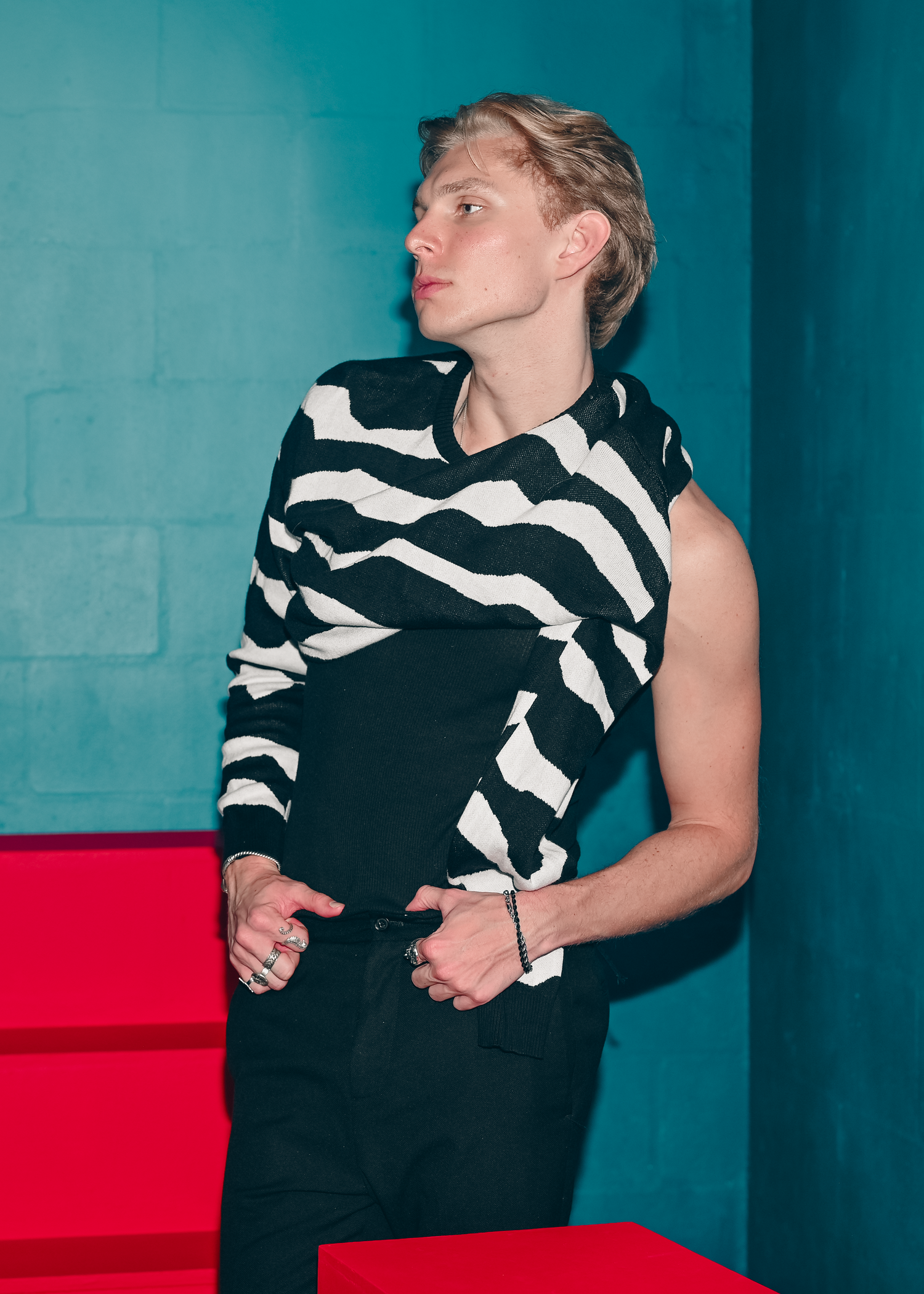 Figure in black and white geometric print poses dramatically against turquoise wall.
