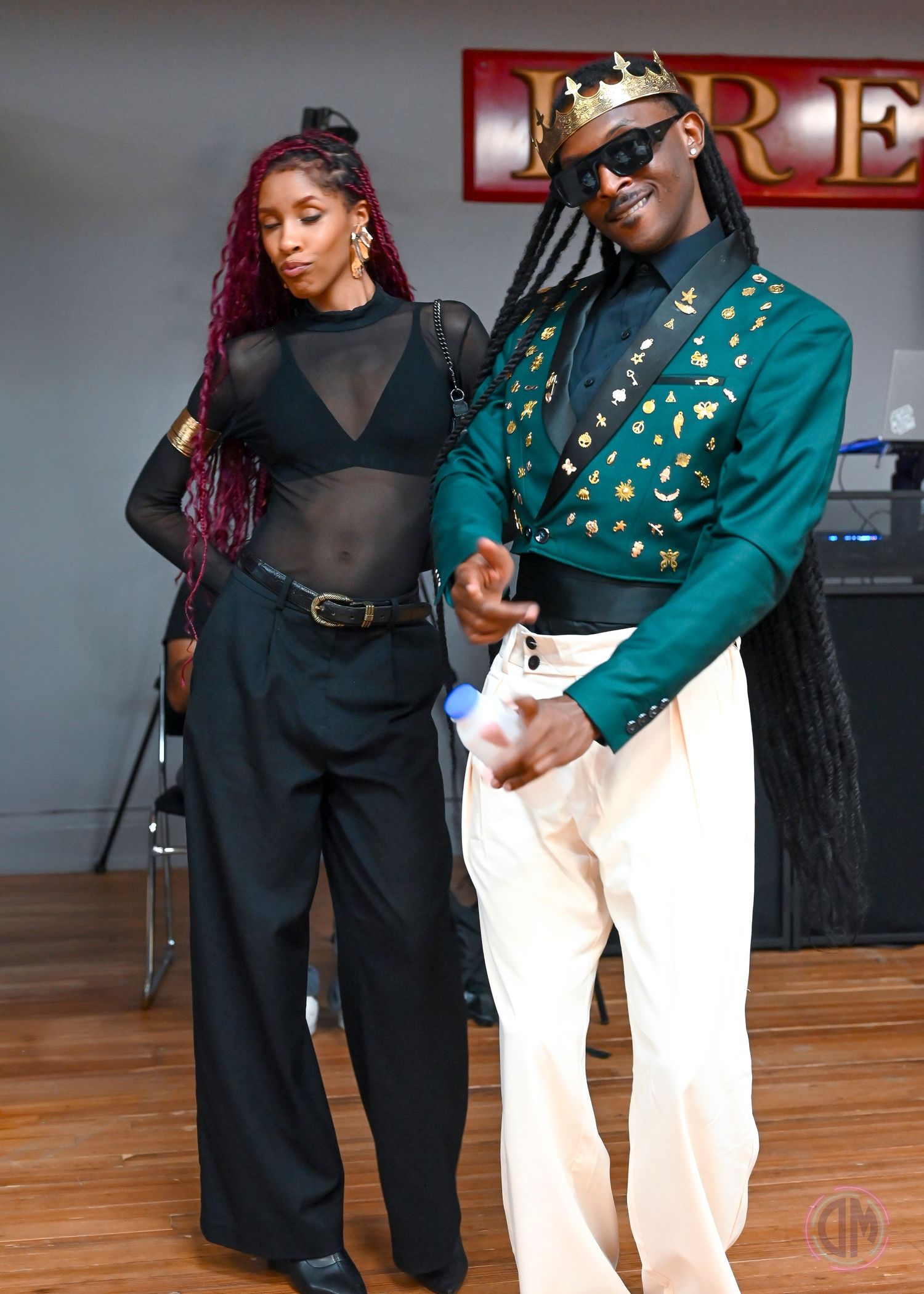 Two dancers perform together on a wooden floor in contrasting black and green outfits.