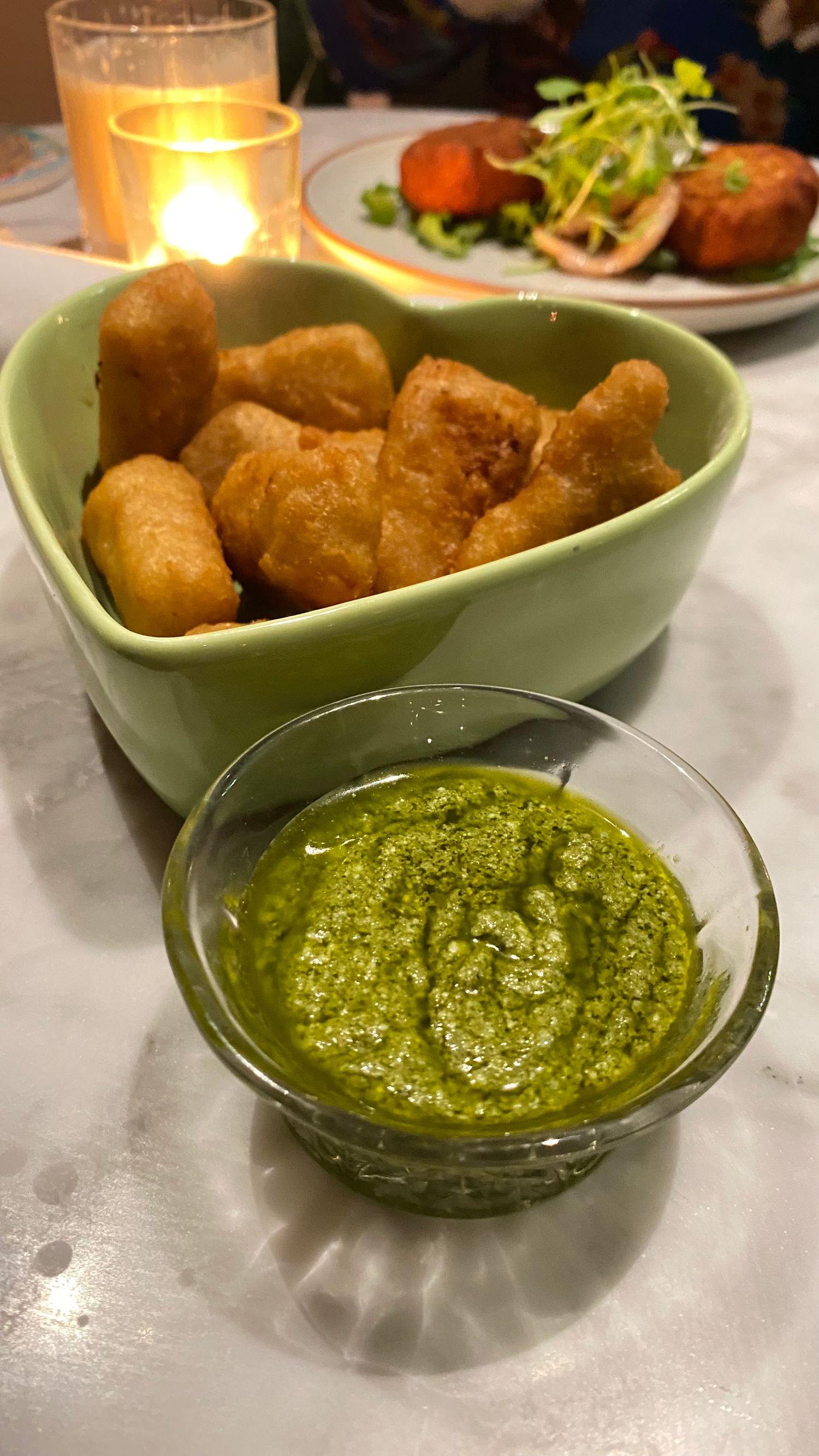 Golden fried appetizers served with vibrant green pesto dipping sauce in small ceramic bowls.