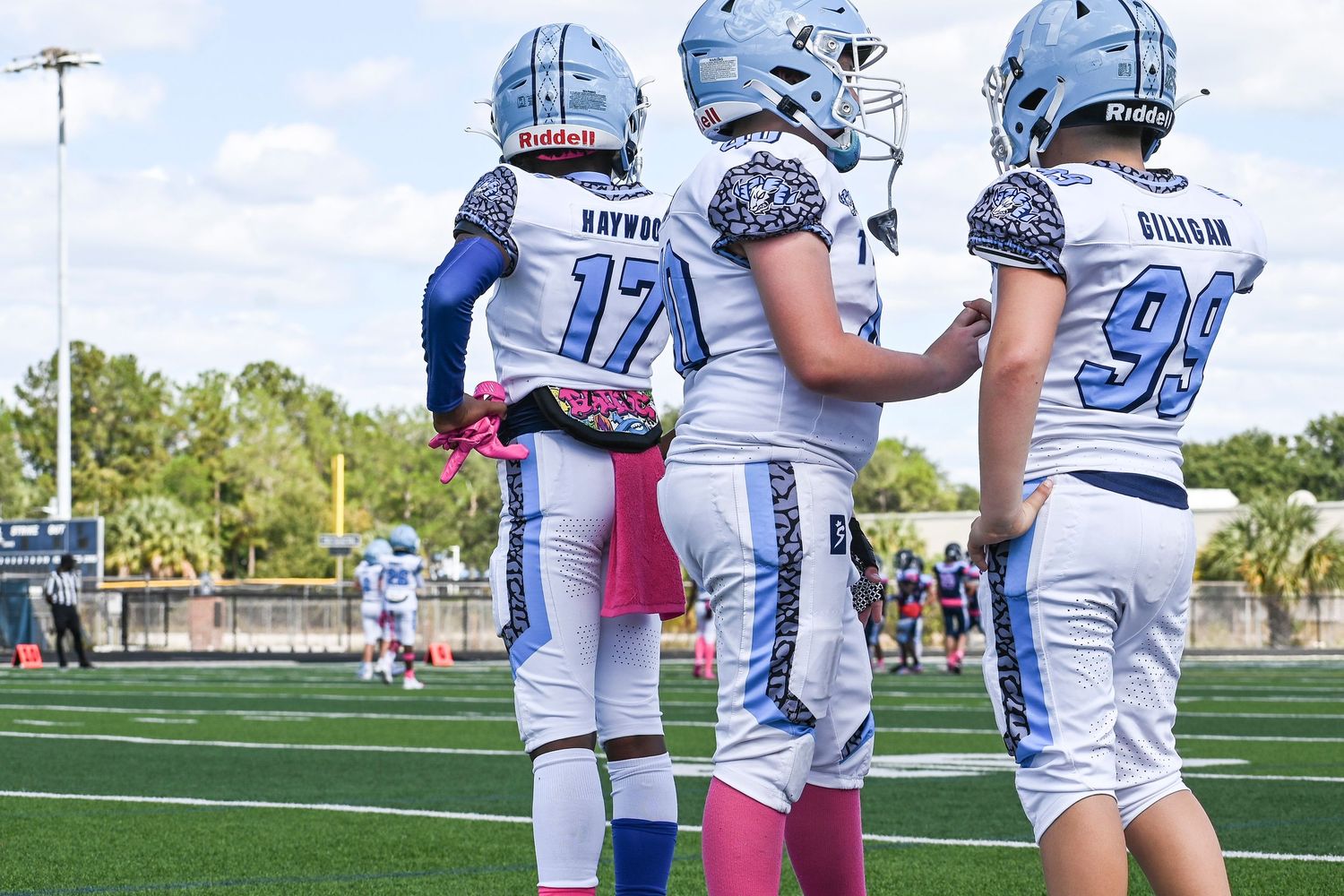 Football players in light blue uniforms lined up on sunny field.