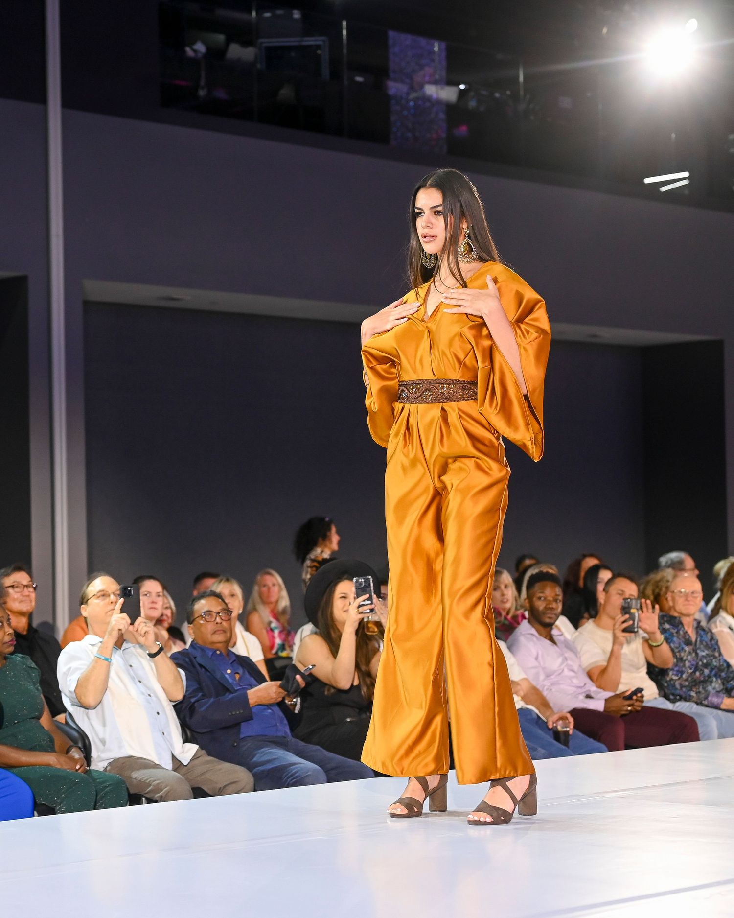 Fashion show featuring orange ensemble on illuminated white catwalk.