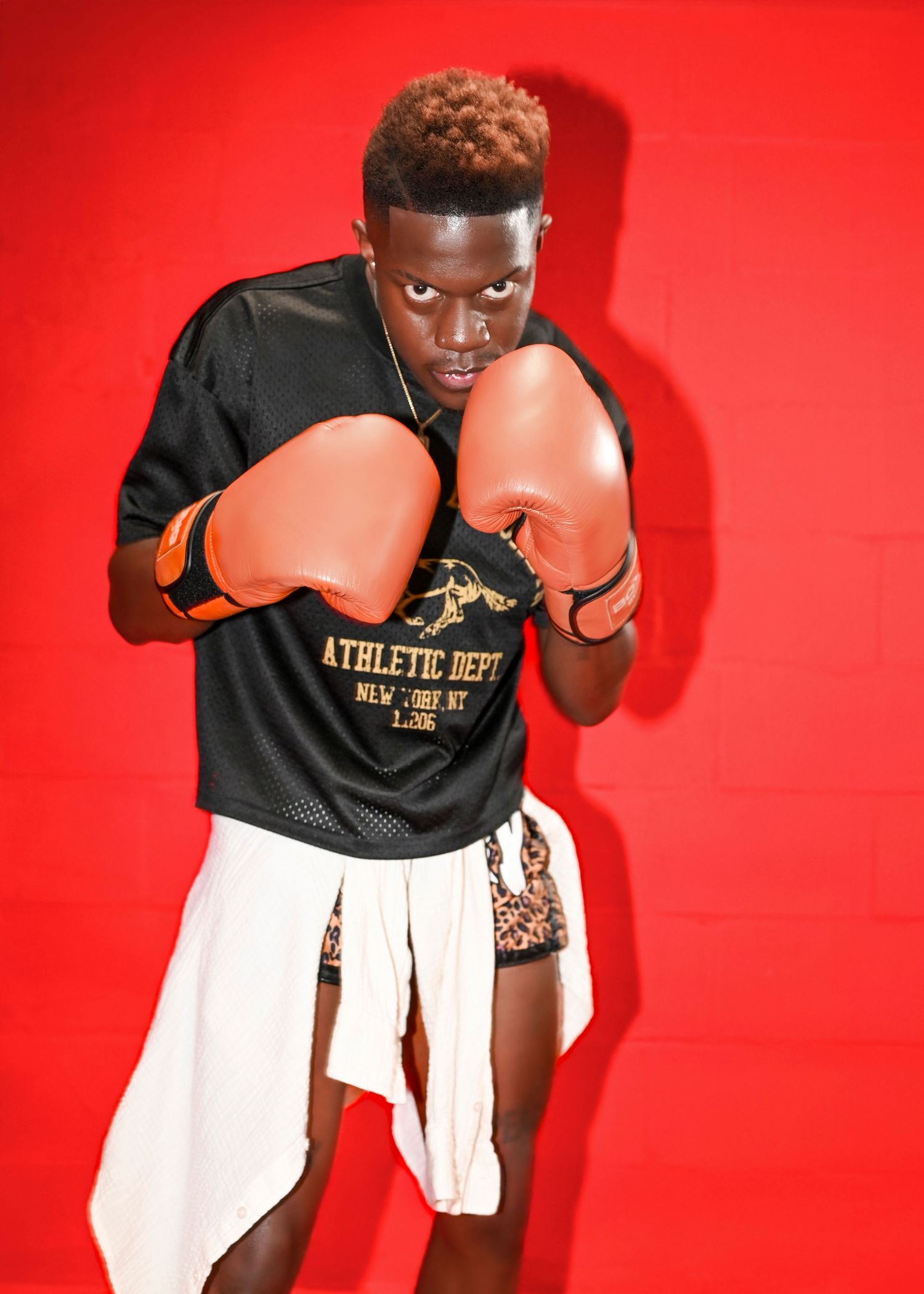 Boxer in athletic department jersey demonstrates fighting stance against red backdrop.