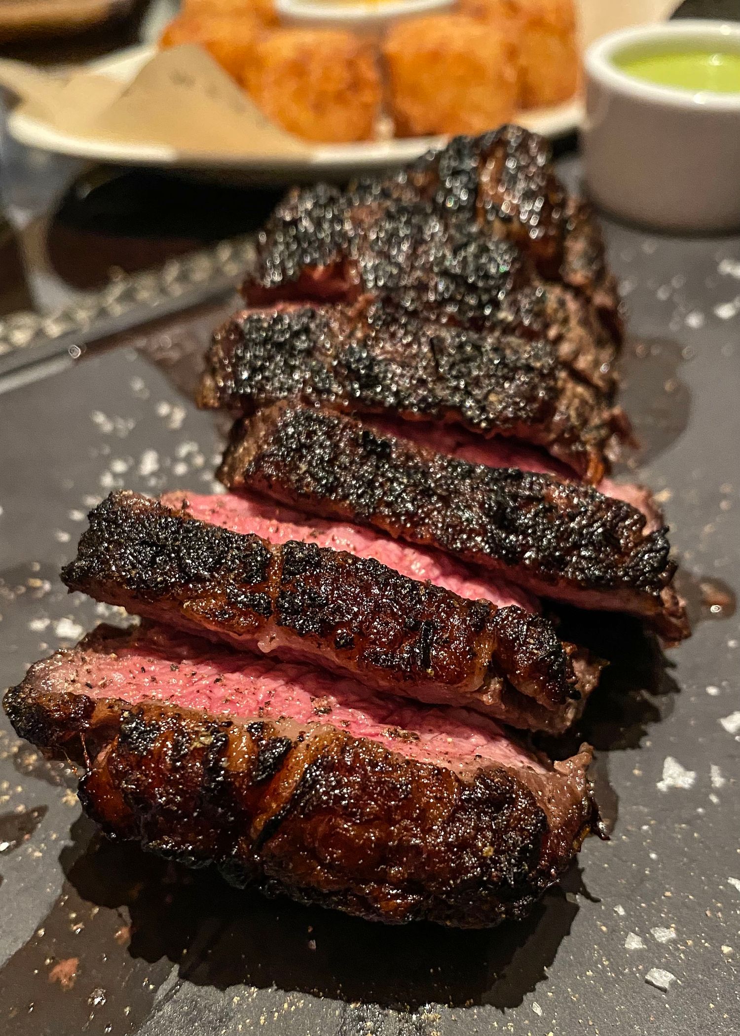 Sliced medium-rare steak with a peppery crust served on a dark plate.