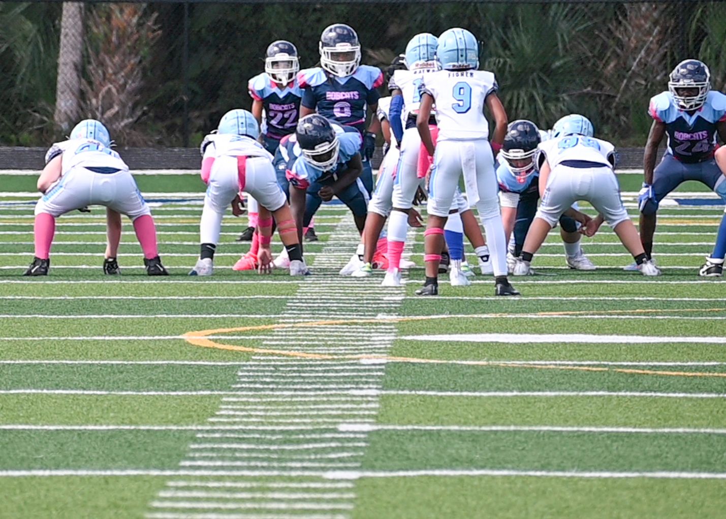 Football players lined up in formation on artificial turf field.