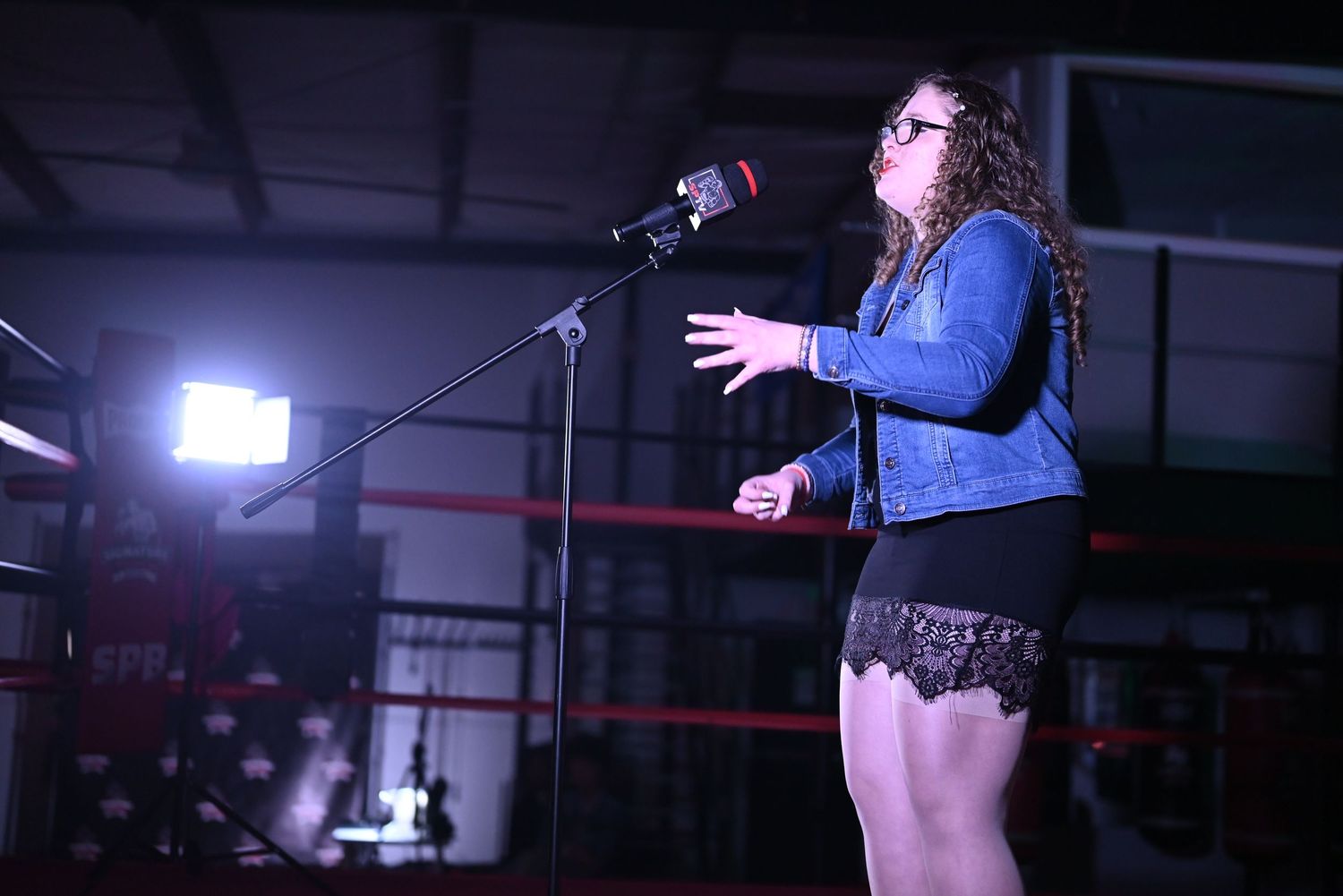 Stage performance captured in dramatic lighting with performer silhouetted against blue background.
