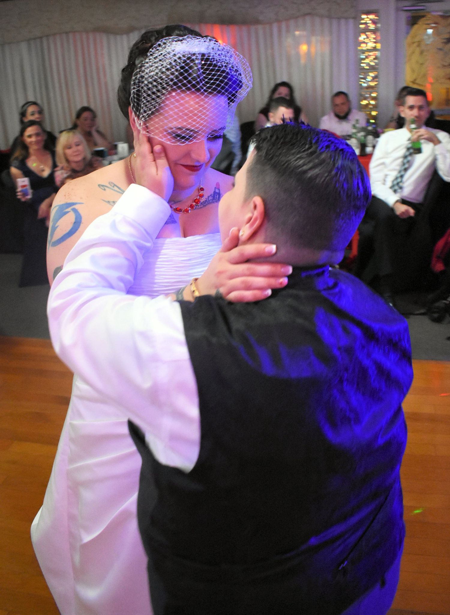 Bride and groom share an emotional first dance at their wedding reception, surrounded by guests under blue lighting.
