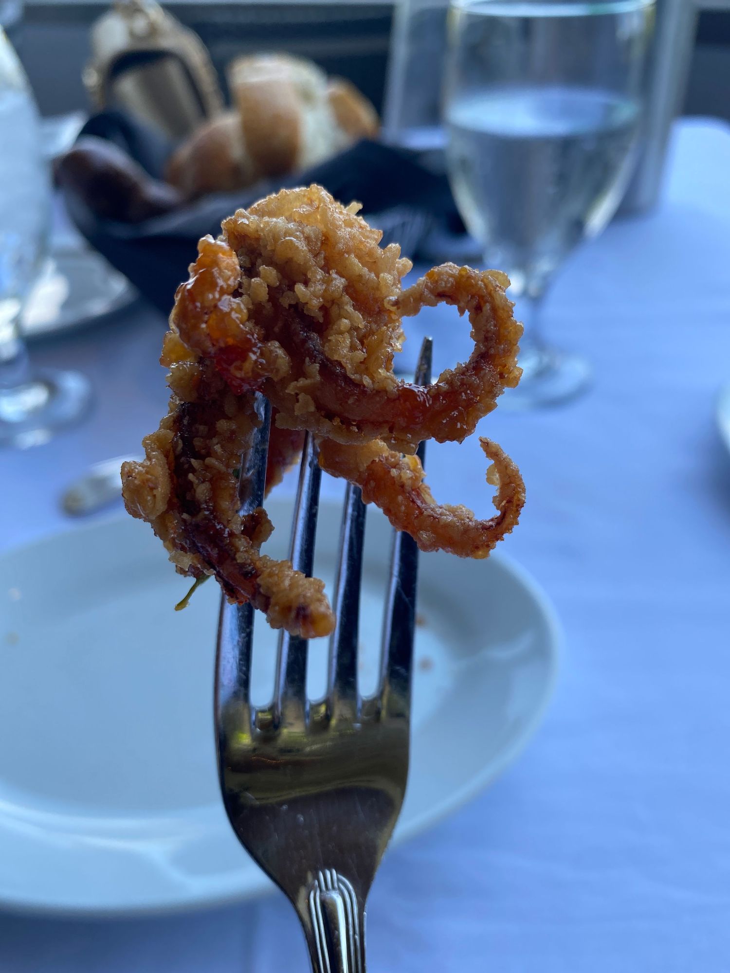Crispy fried calamari rings held up by a silver fork against a white plate.