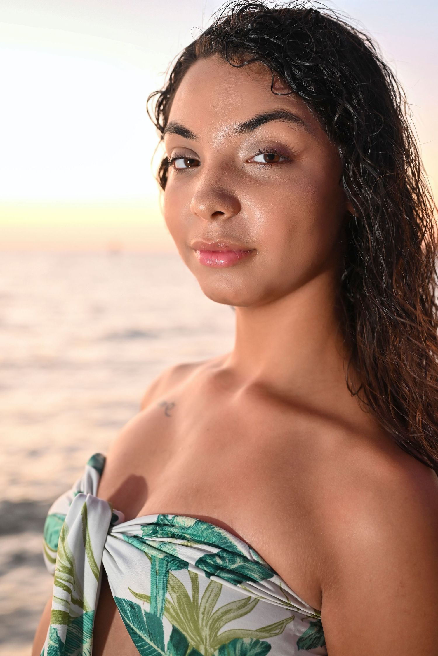 Portrait at sunset wearing a tropical print dress with natural curly hair against a beach backdrop.