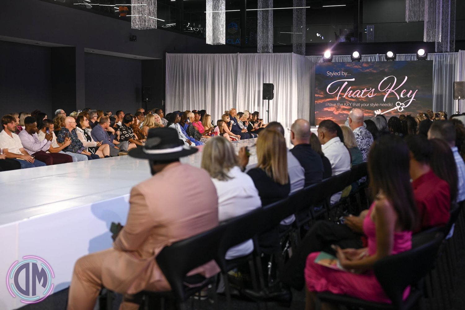 Fashion week event space with filled audience seating and illuminated runway stage.