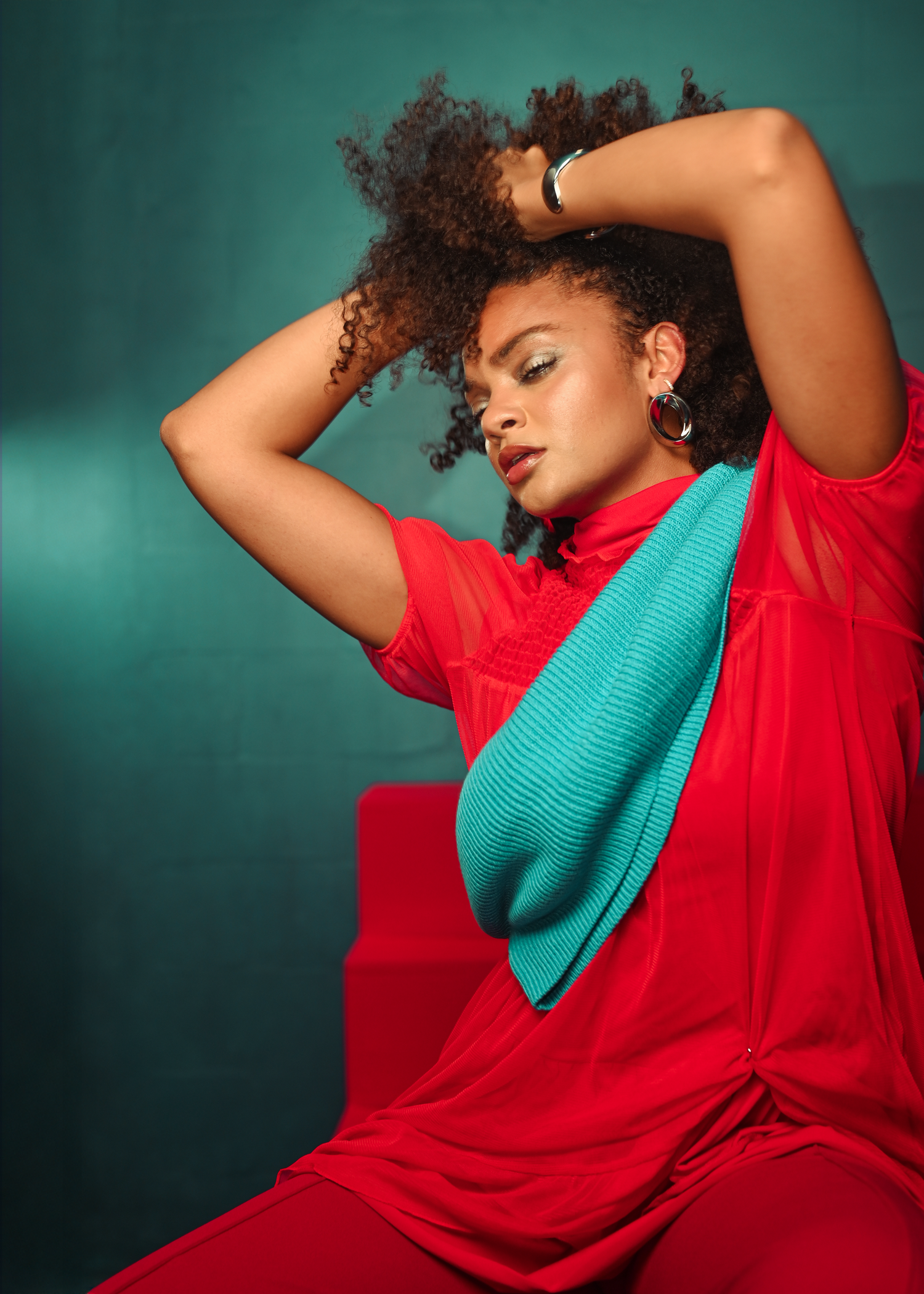 Fashion model in red and turquoise poses dramatically against dark green backdrop.